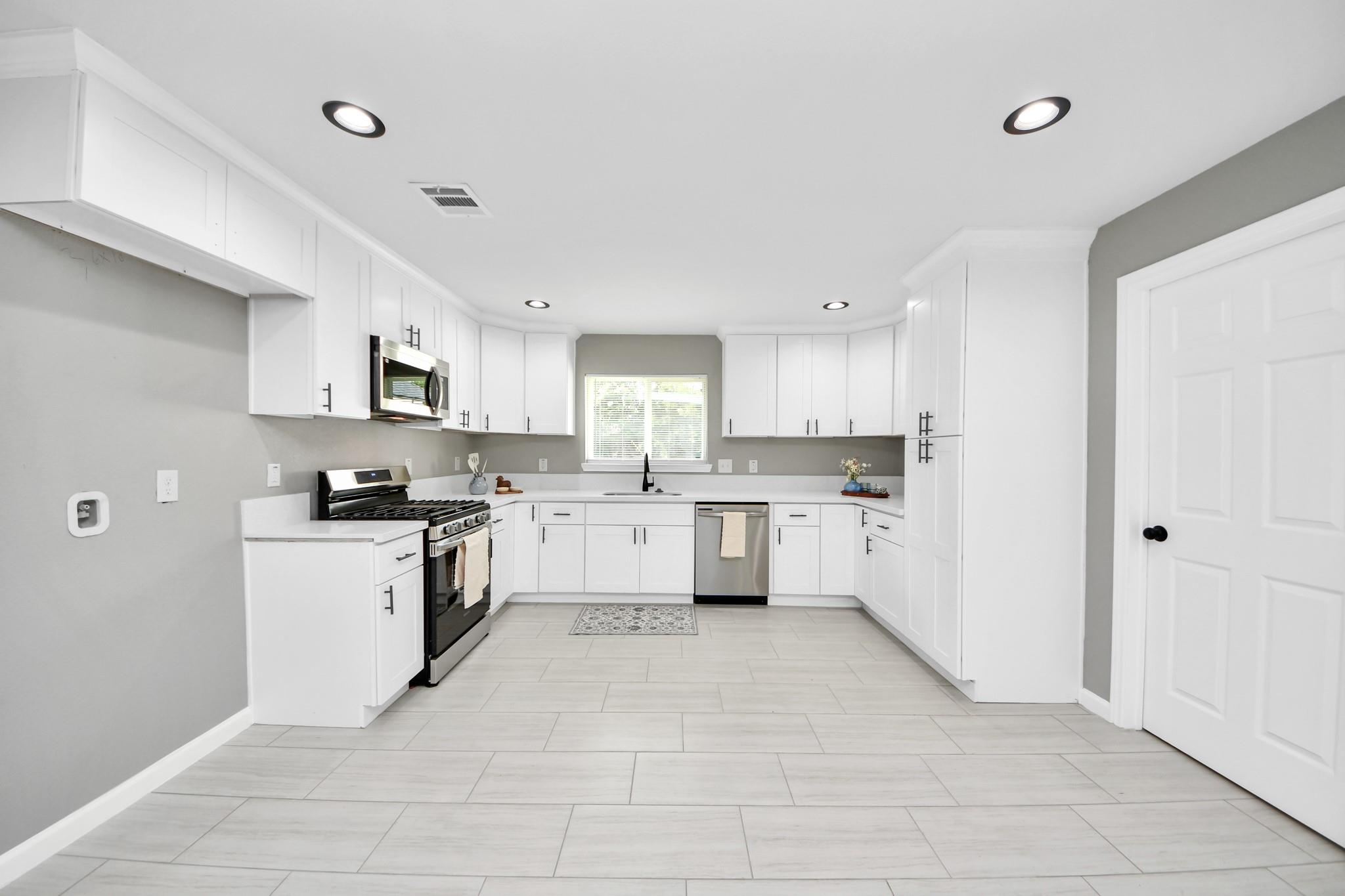 Bright kitchen with white cabinets, stainless steel appliances, and large light tile flooring.