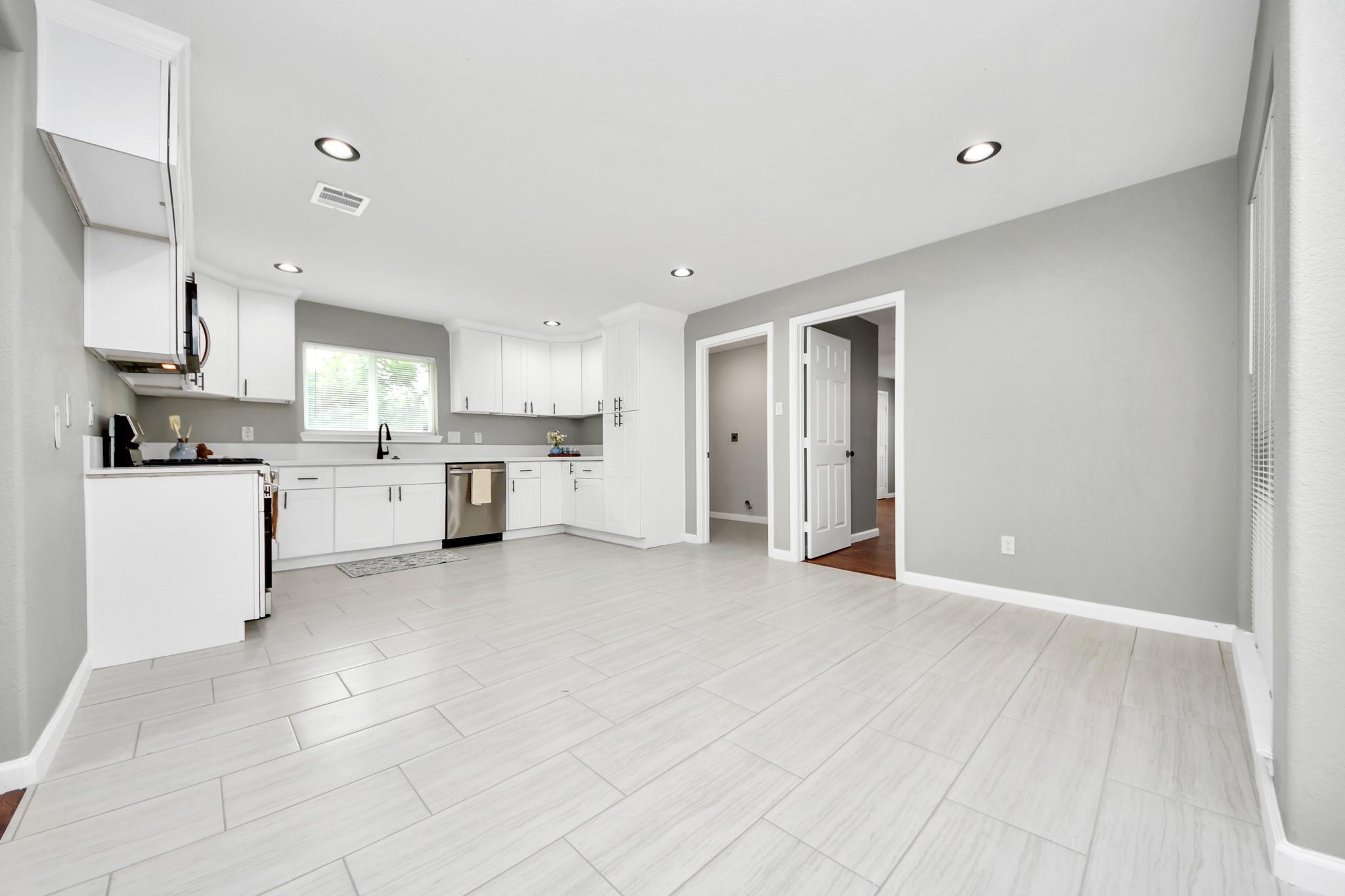 Kitchen with white cabinetry, stainless-steel appliances, and large pale tile flooring.