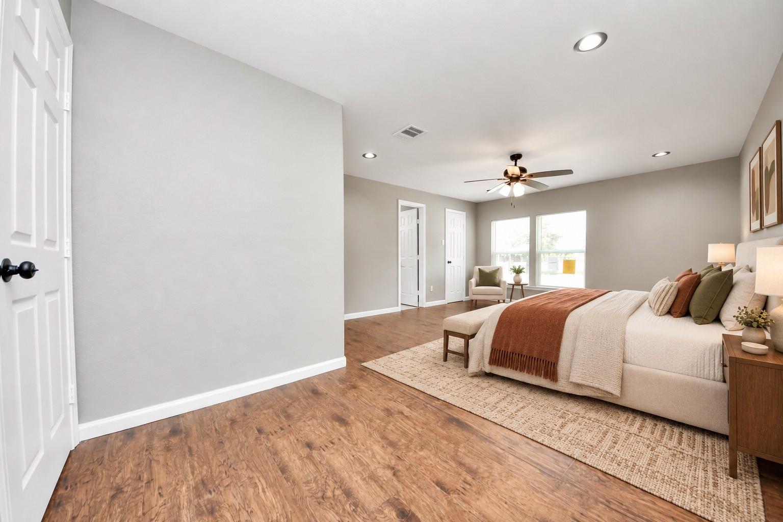 Staged bedroom with a large white bed, rust-colored throw, wood floors, and ceiling fan.