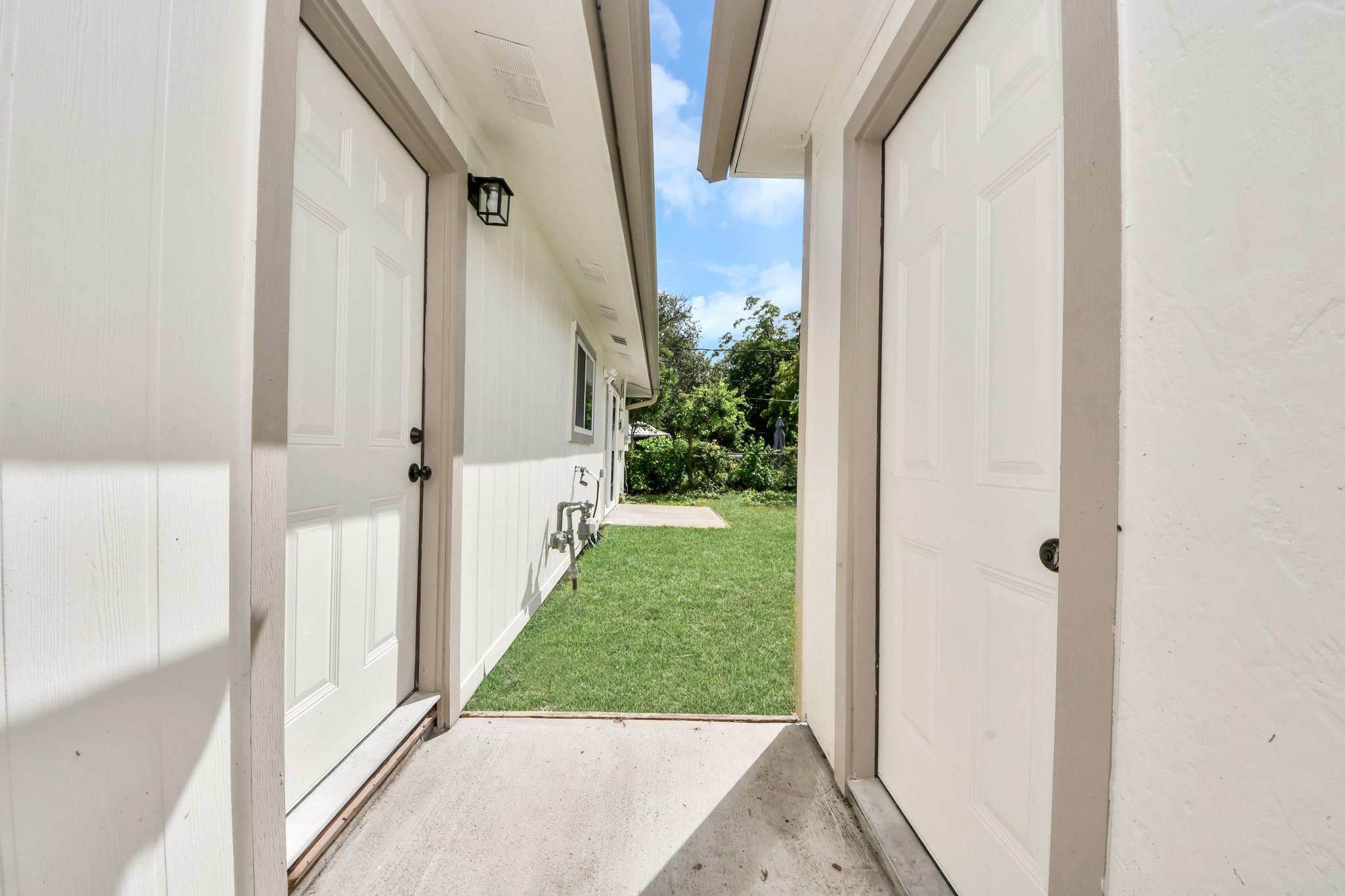 Side passage with two white doors opening onto a narrow grassy yard.