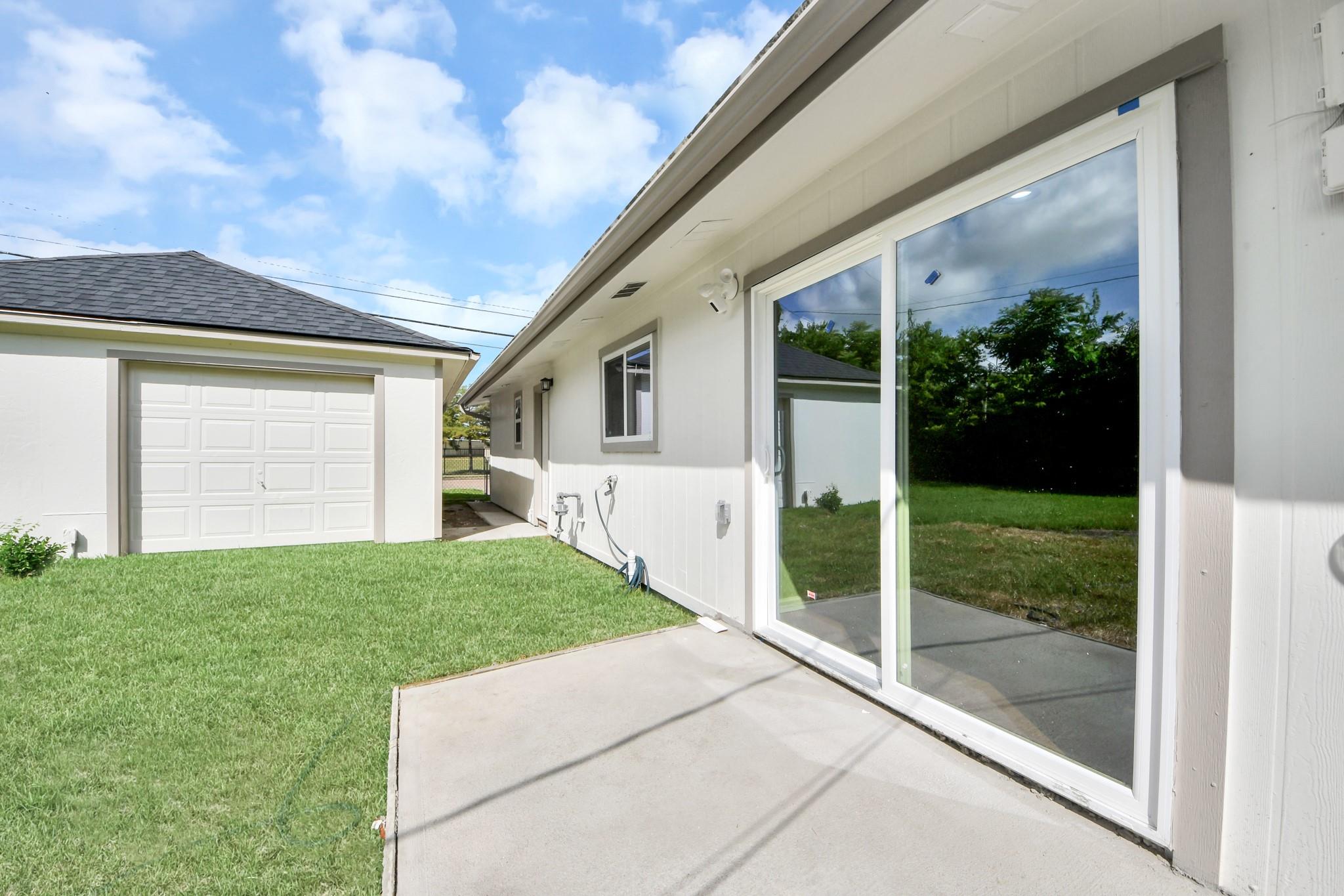 House exterior with a concrete patio, large sliding glass doors, lawn, and detached garage.