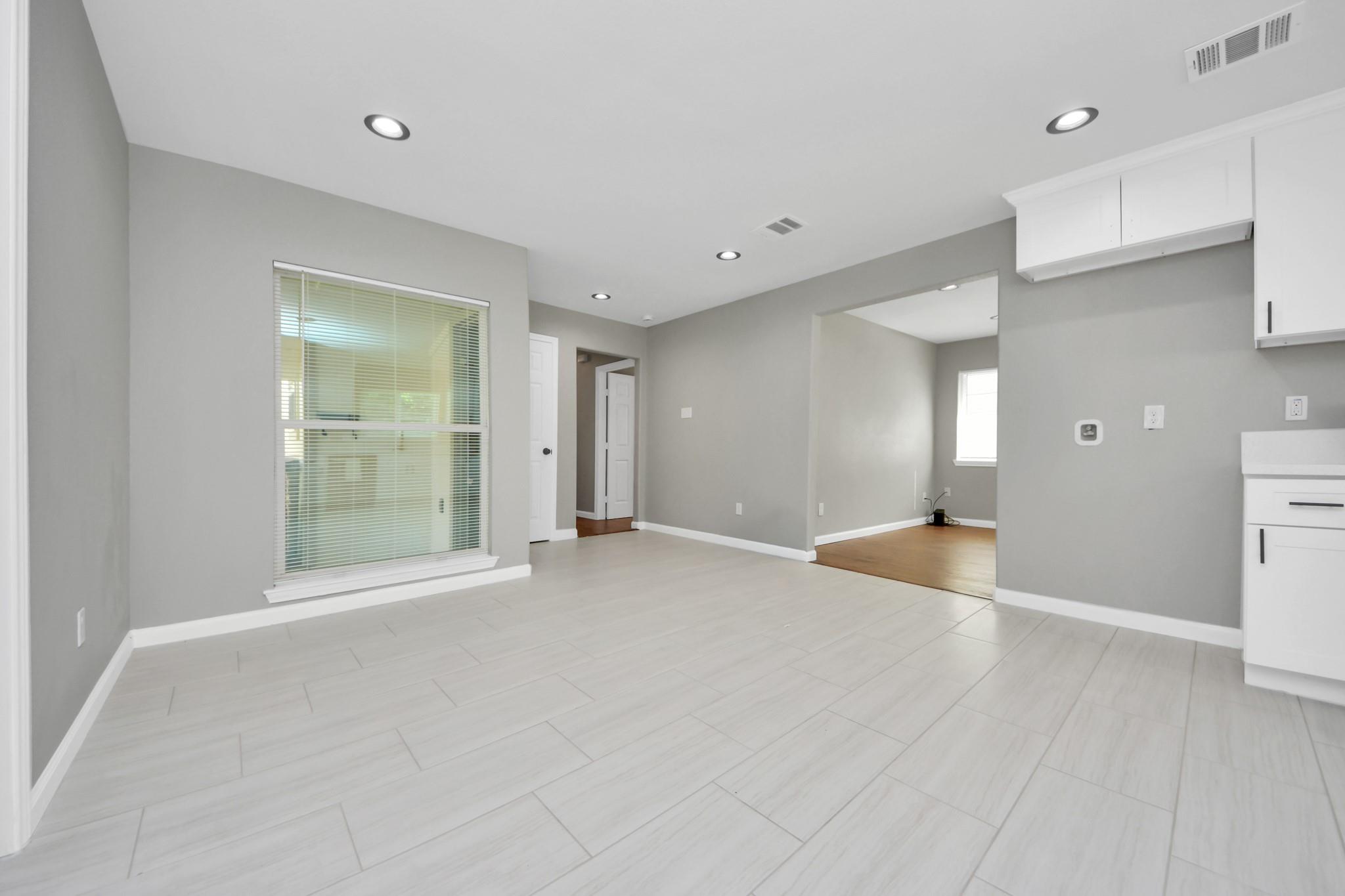 Vacant open-plan kitchen and living area with gray walls, white cabinets, and light tile flooring.