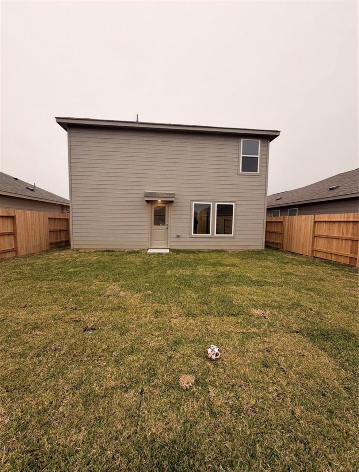 Two-story gray house behind a fenced lawn, with a soccer ball in the backyard.