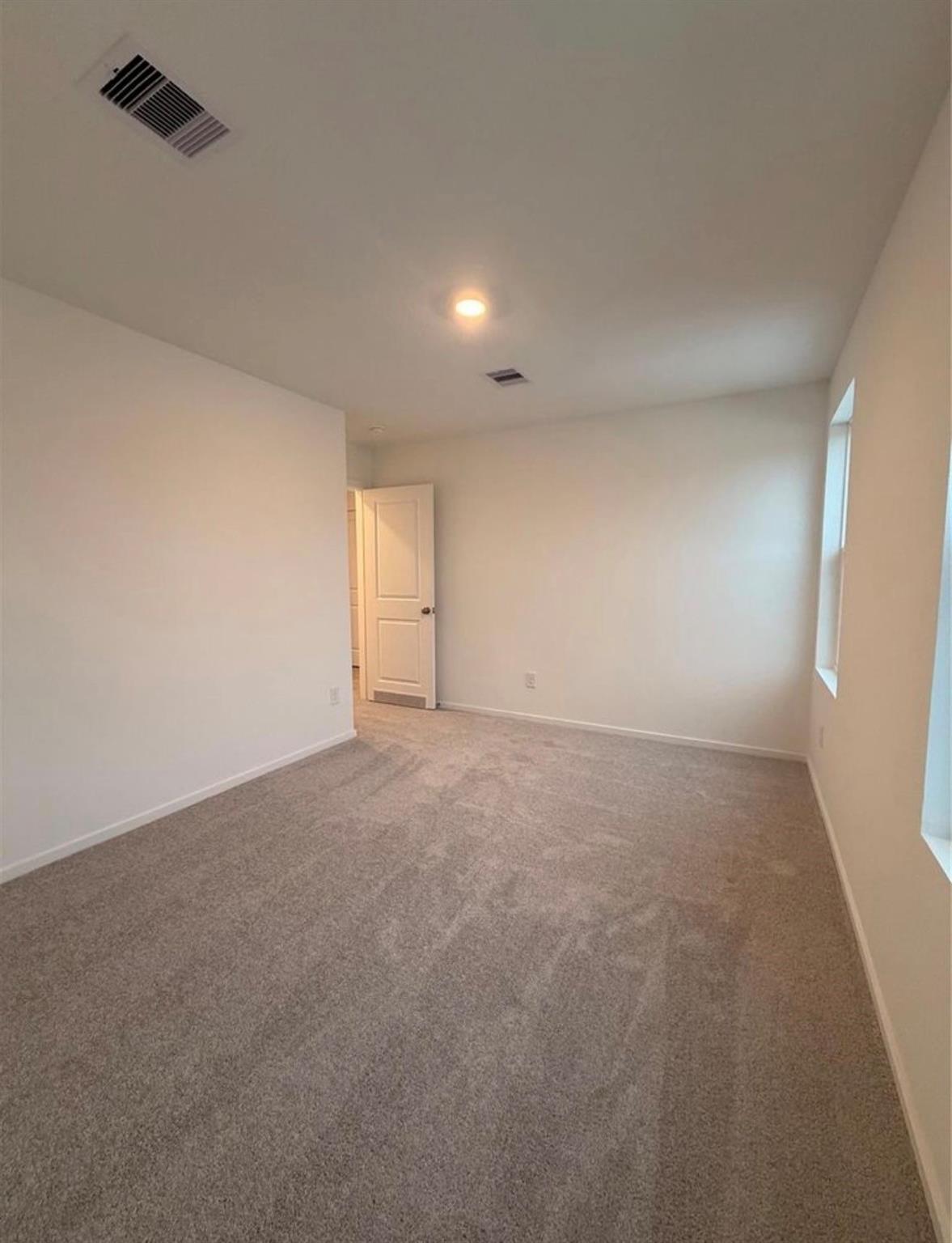Empty carpeted bedroom with white walls, two narrow windows, and an open door.