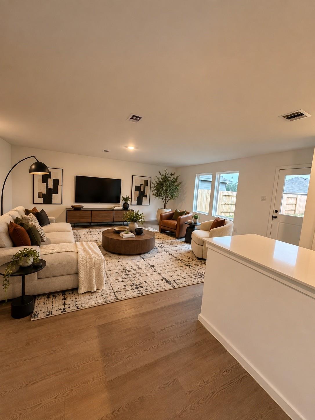 Staged living room with a cream sectional, leather chairs, patterned rug, and kitchen island.