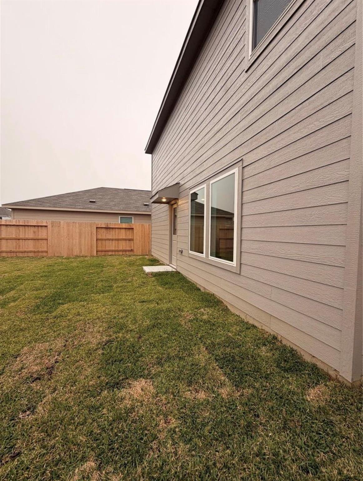 Home’s gray-sided exterior beside a fenced backyard and patchy lawn.