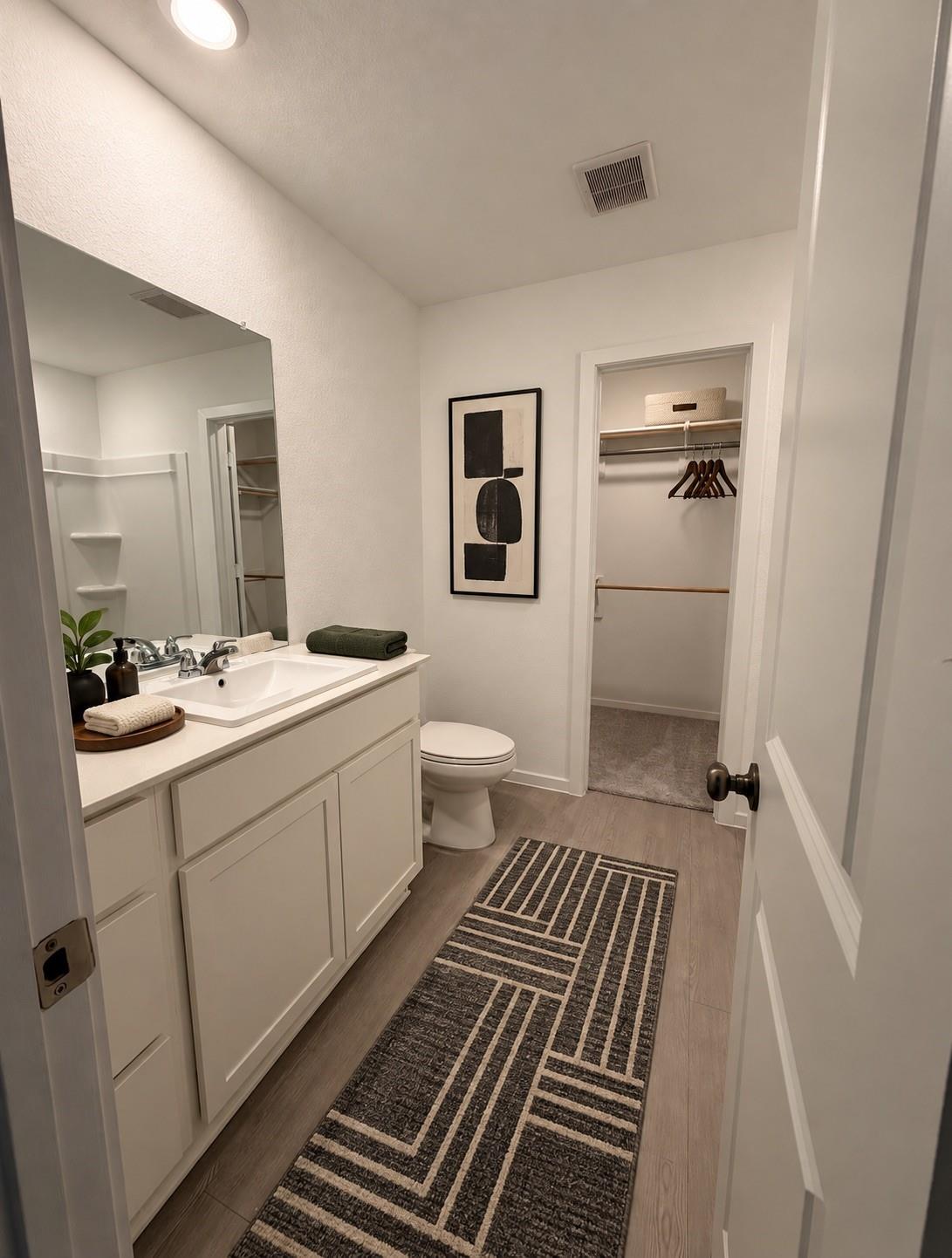 Bathroom with a white vanity, geometric runner rug, and doorway to a walk-in closet.