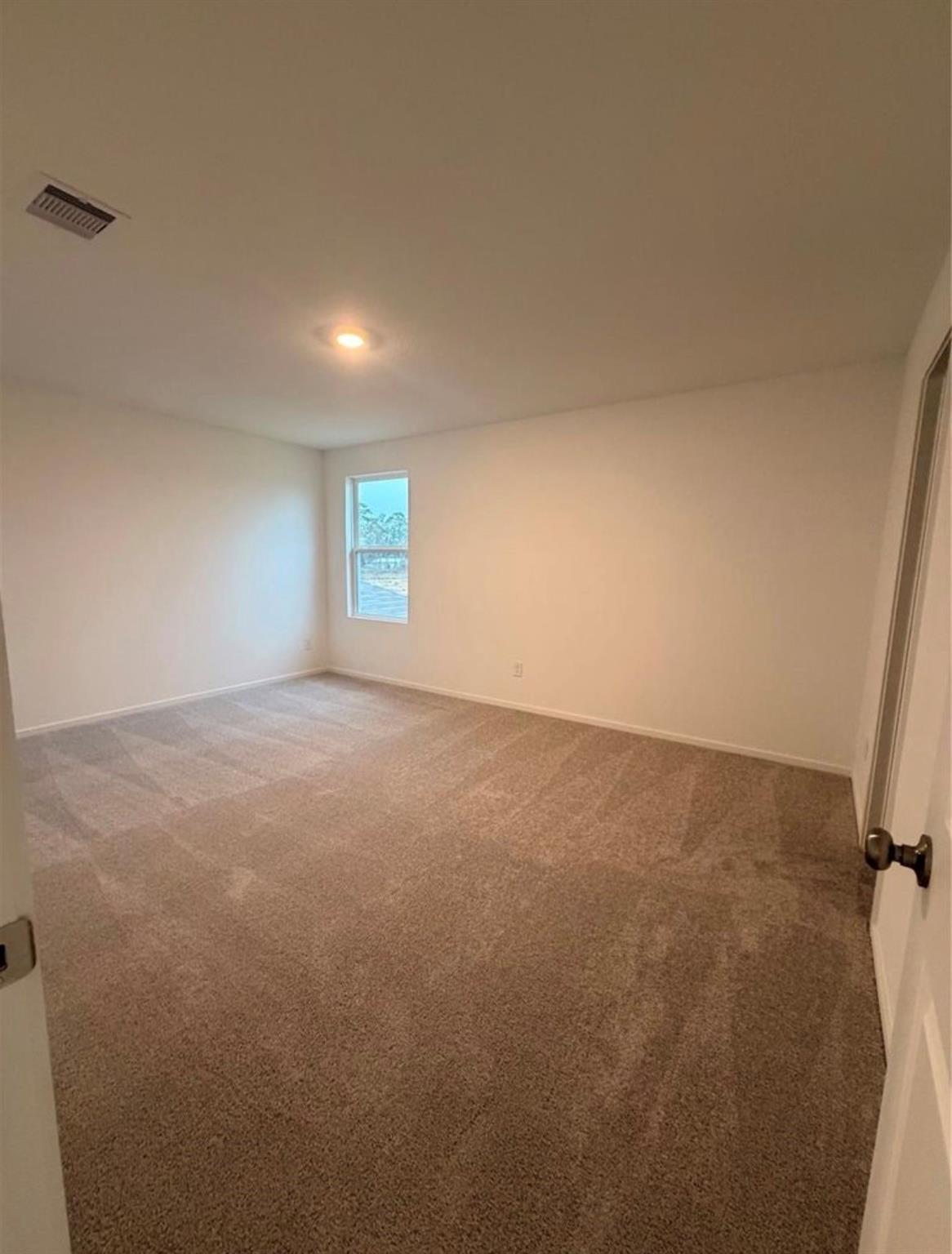 Empty bedroom with beige carpet and a single window.