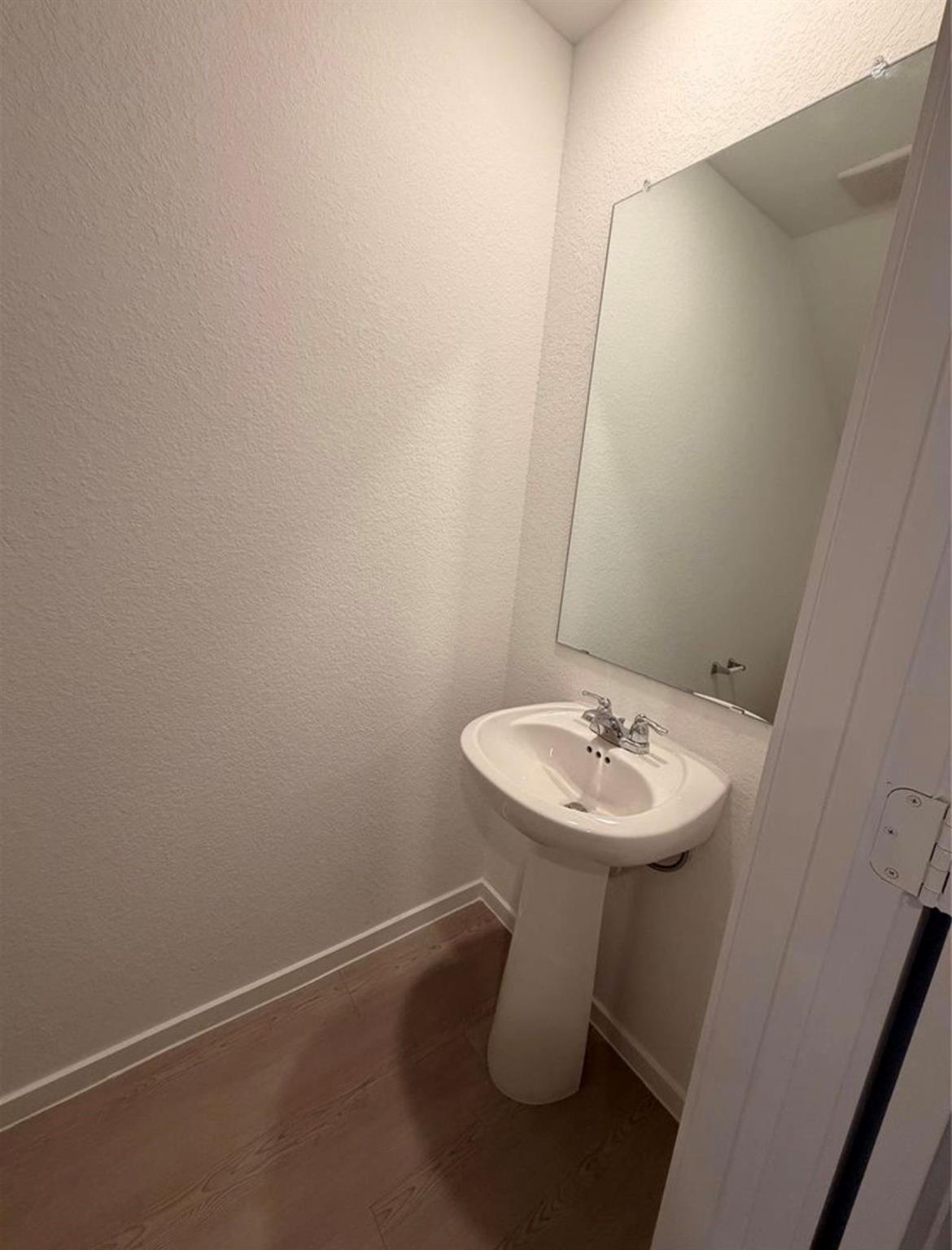 Small bathroom with a white pedestal sink, large mirror, and wood-look flooring.