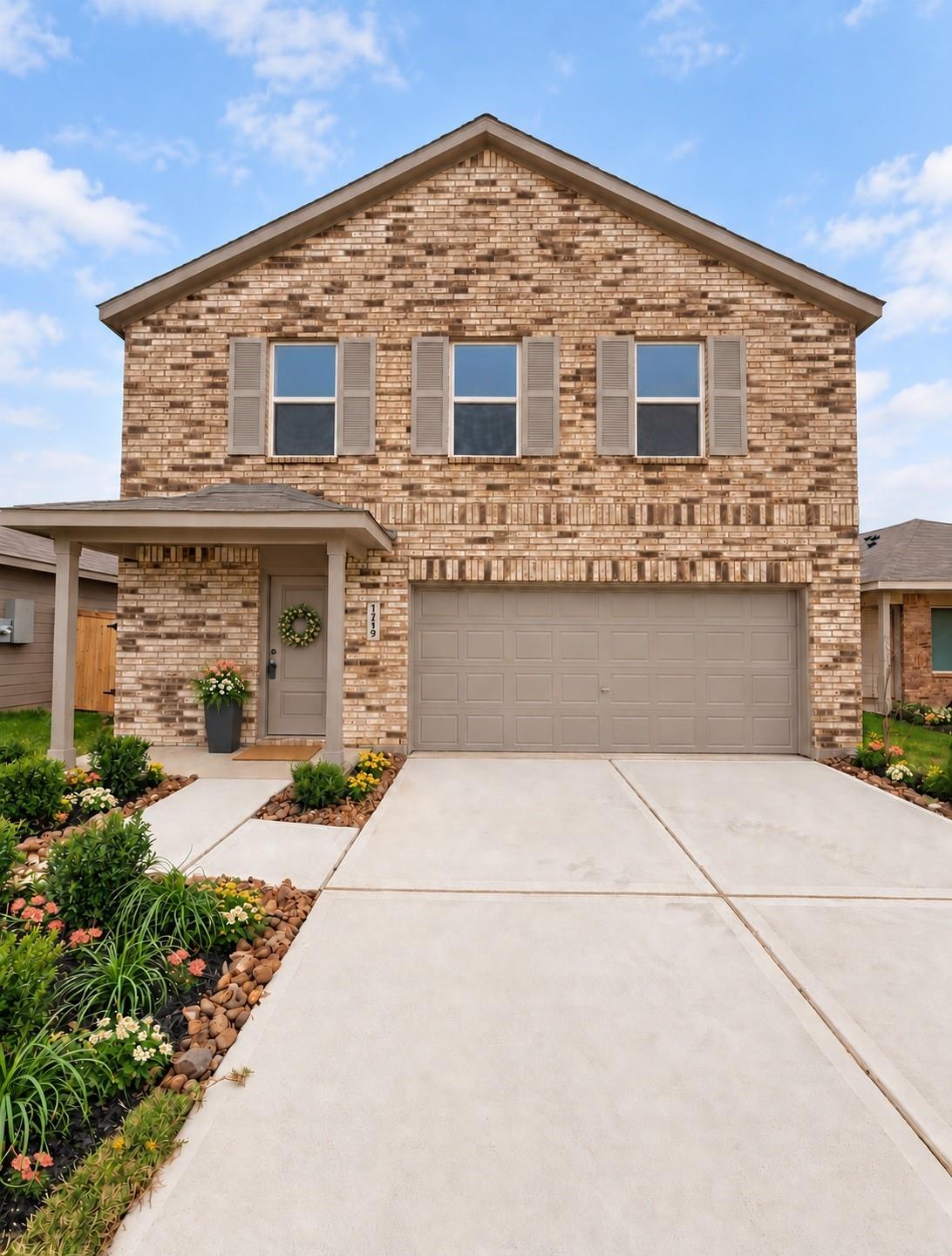 Two-story brick home with an attached garage, covered entry, and landscaped driveway.