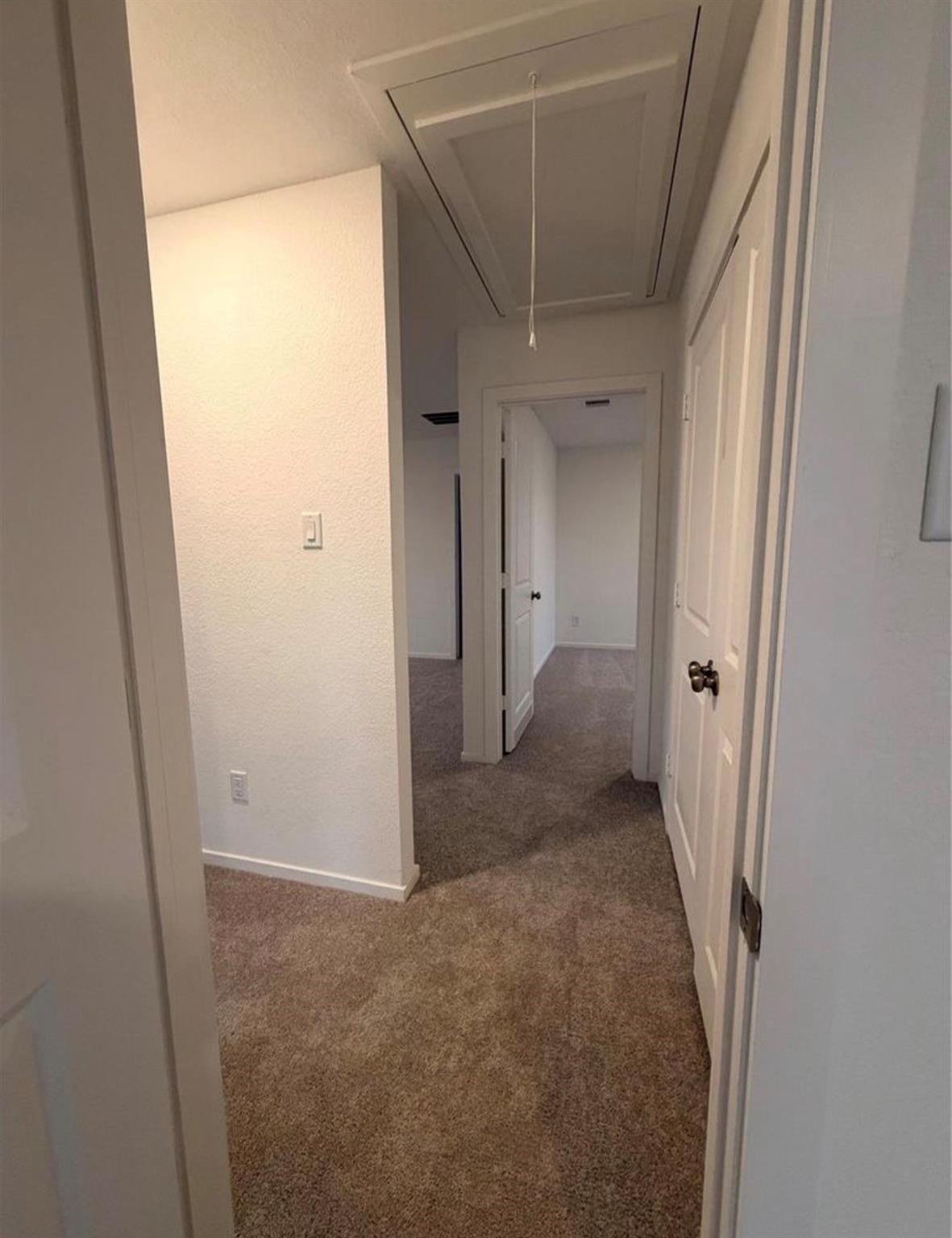 Carpeted hallway with white doors and a ceiling attic access panel.