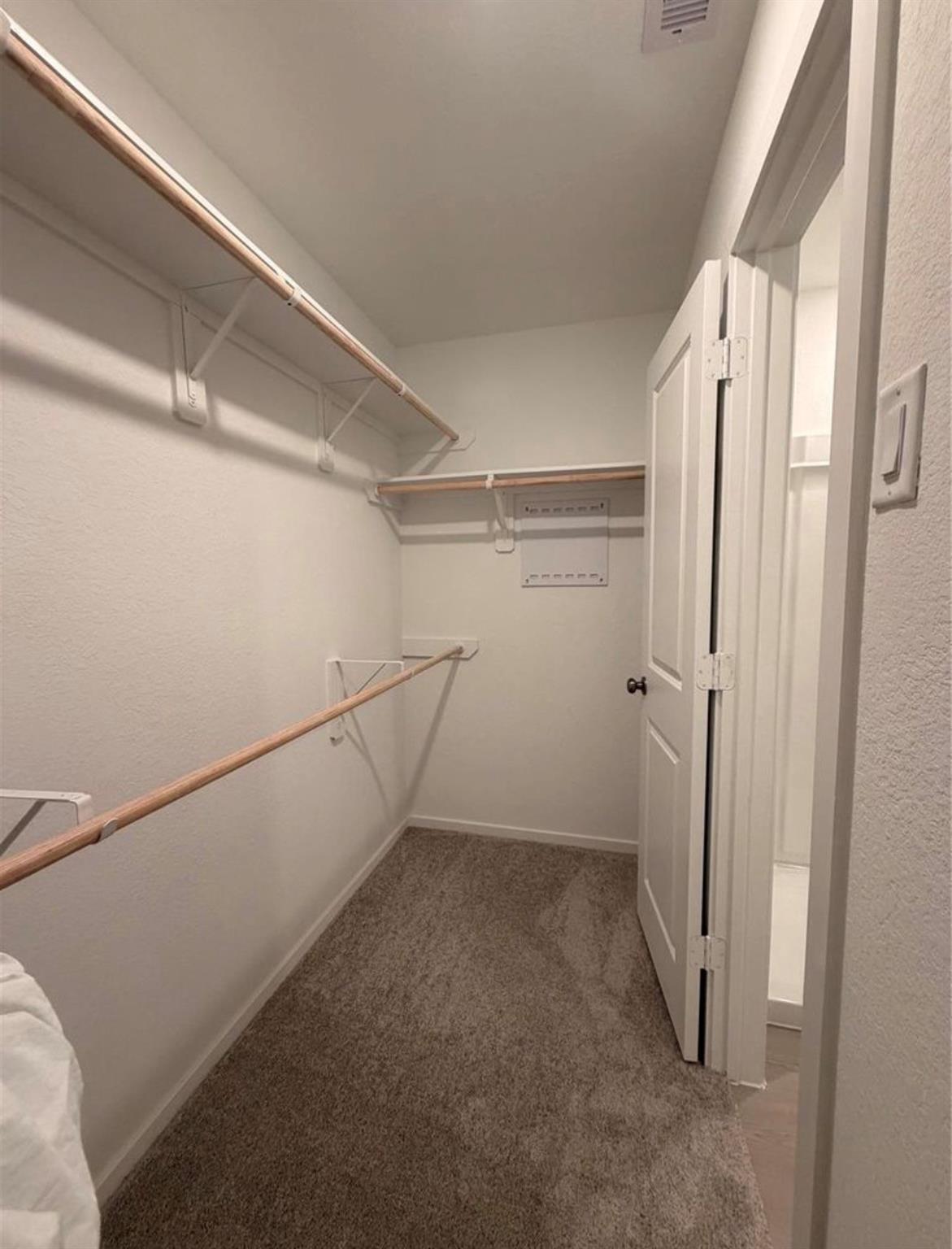 Empty walk-in closet with carpeted floor and wooden hanging rods along three walls.