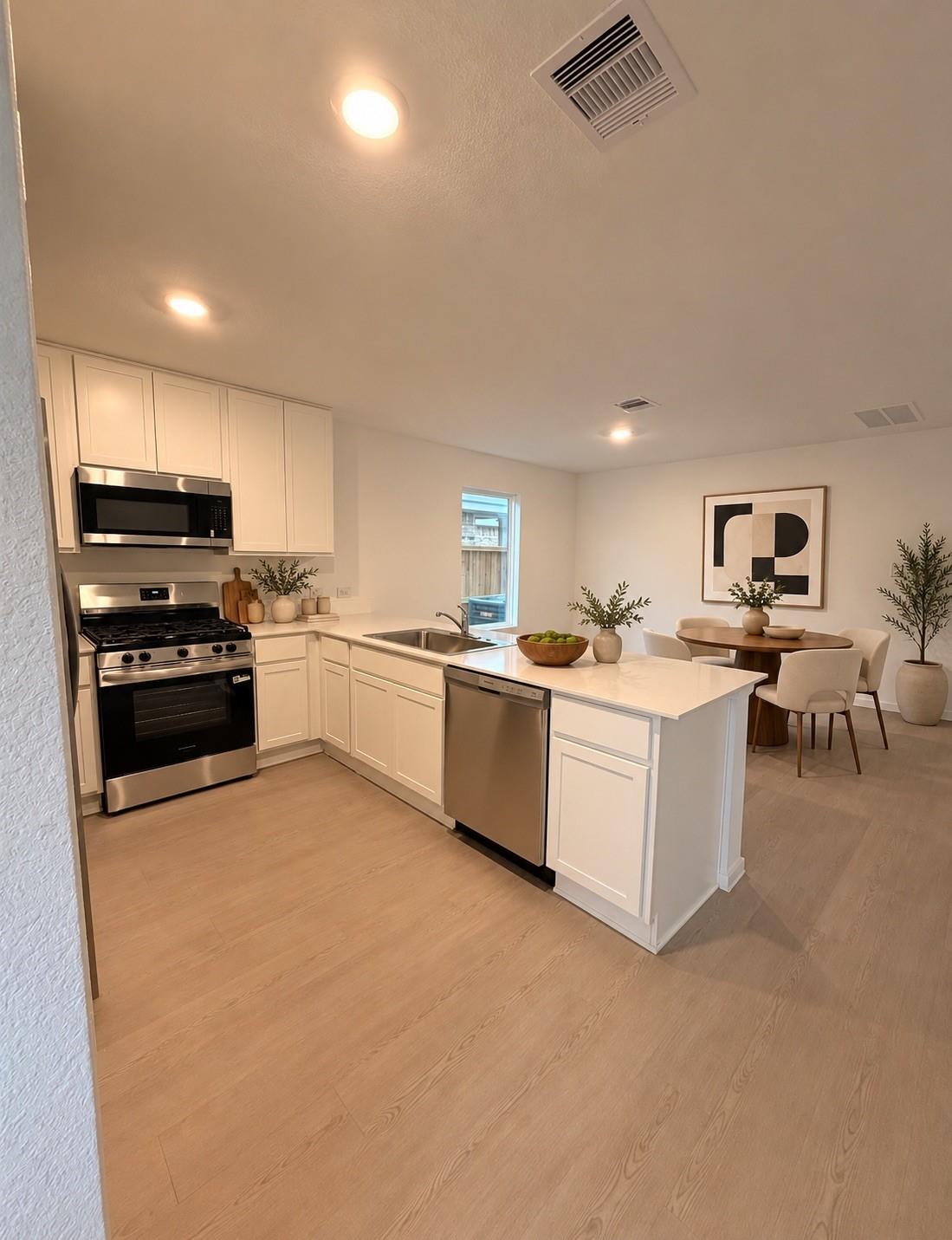 Staged kitchen with white cabinetry, a central island, stainless steel appliances, and an adjacent dining area.