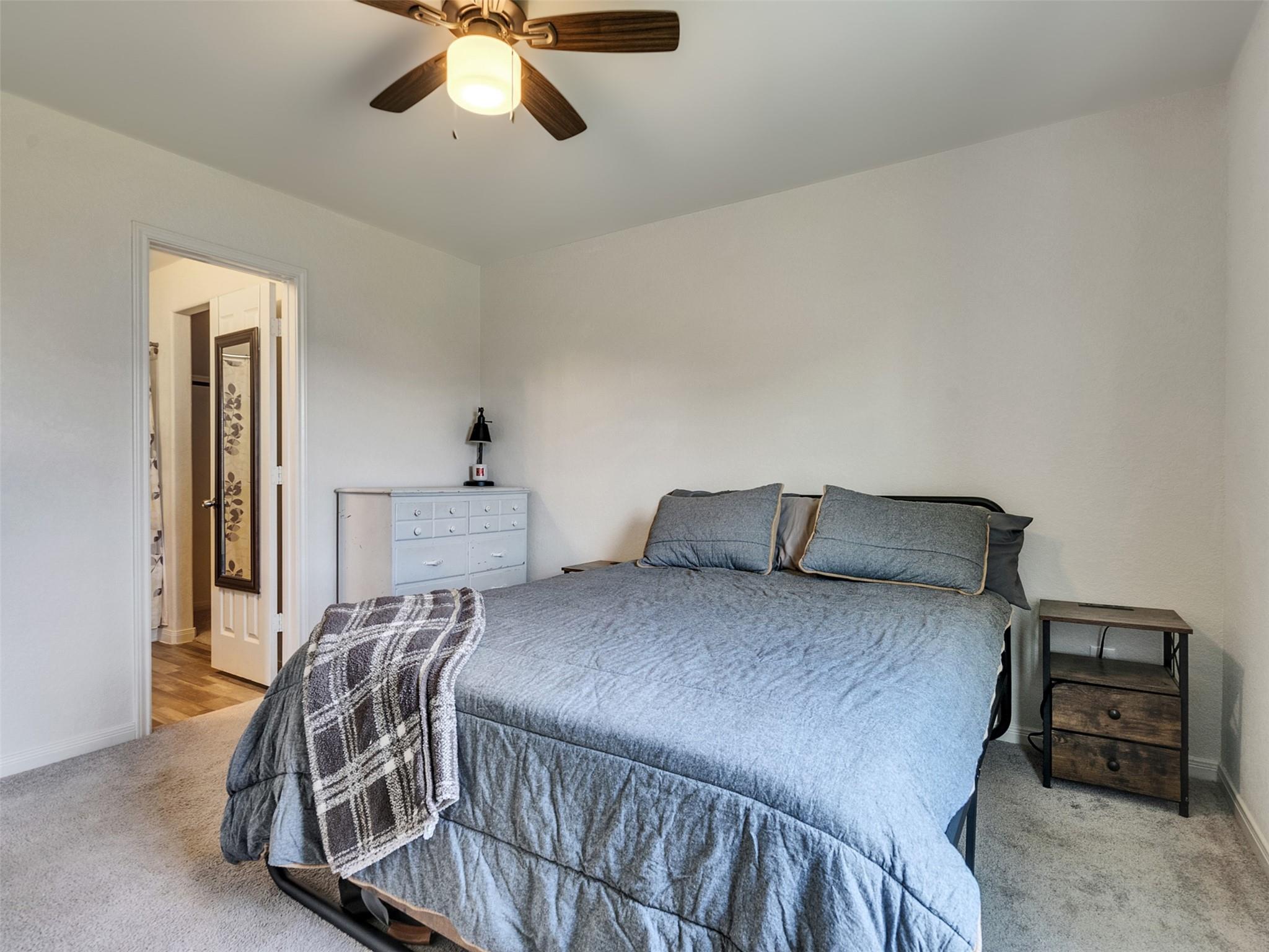Bedroom with a large blue-gray bed, plaid throw, white dresser, and ceiling fan.
