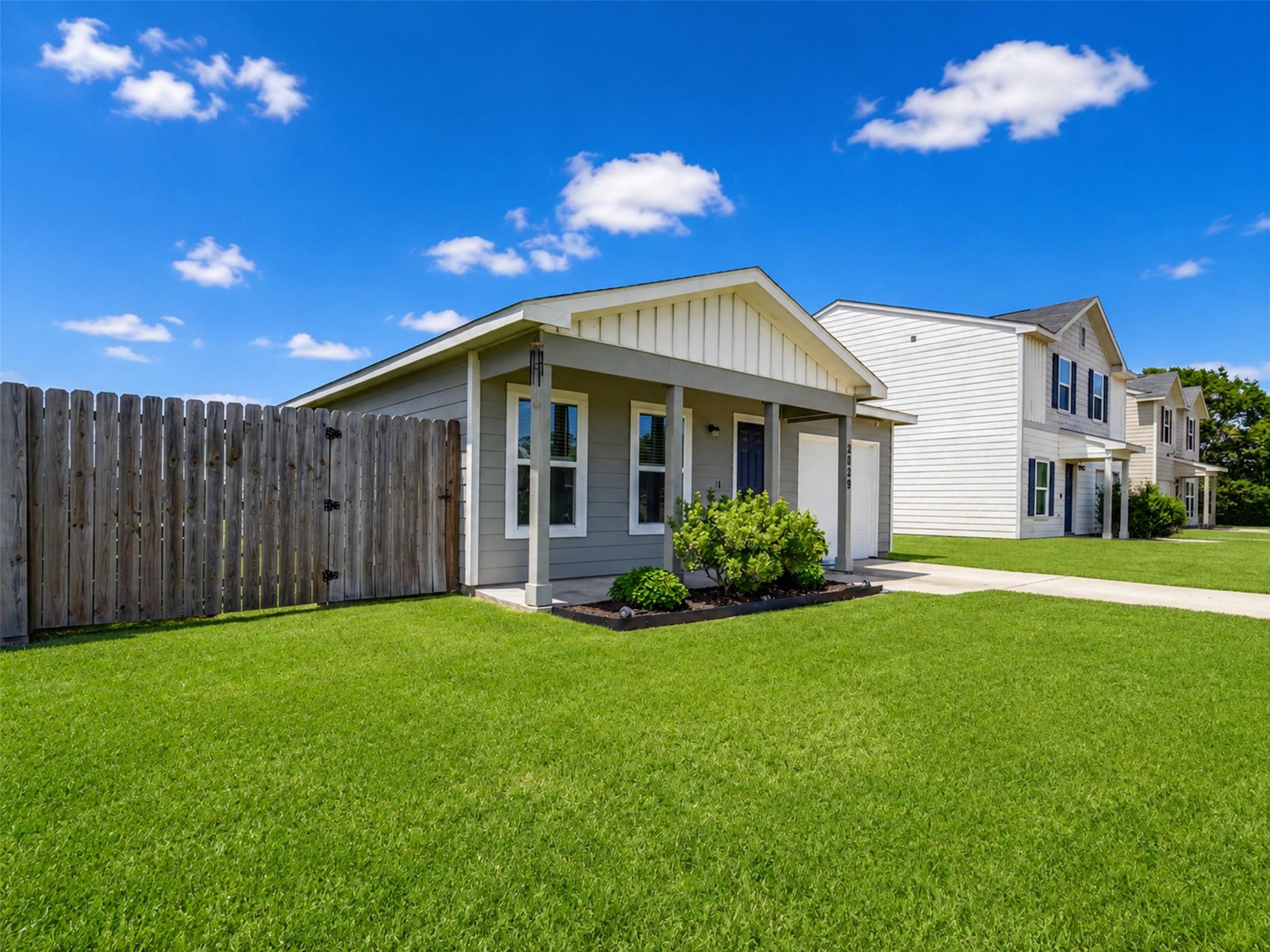 Gray single-story home with a covered porch, blue door, and broad green lawn.
