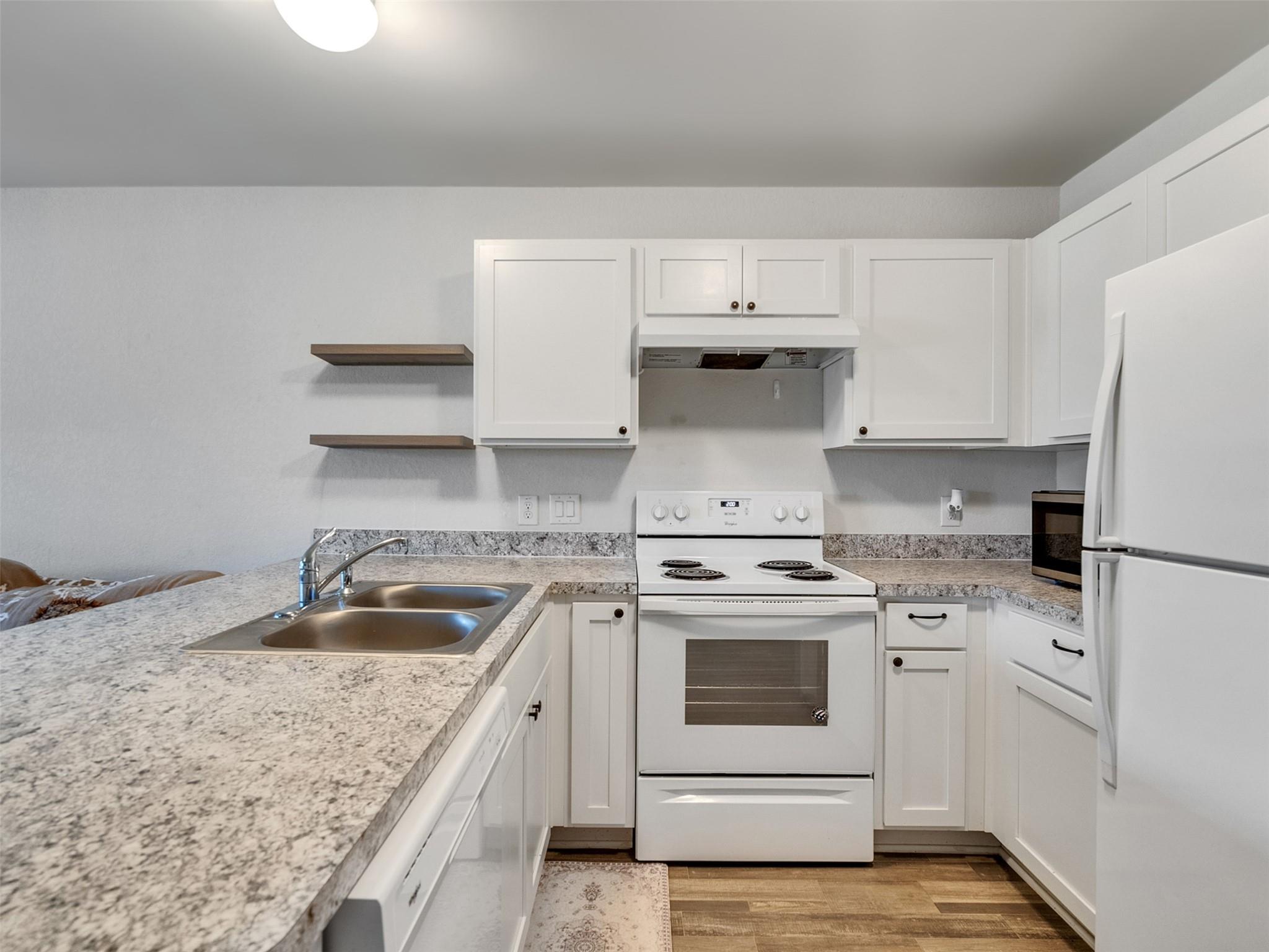 Compact kitchen with white cabinets, granite countertops, double sink, and electric range.