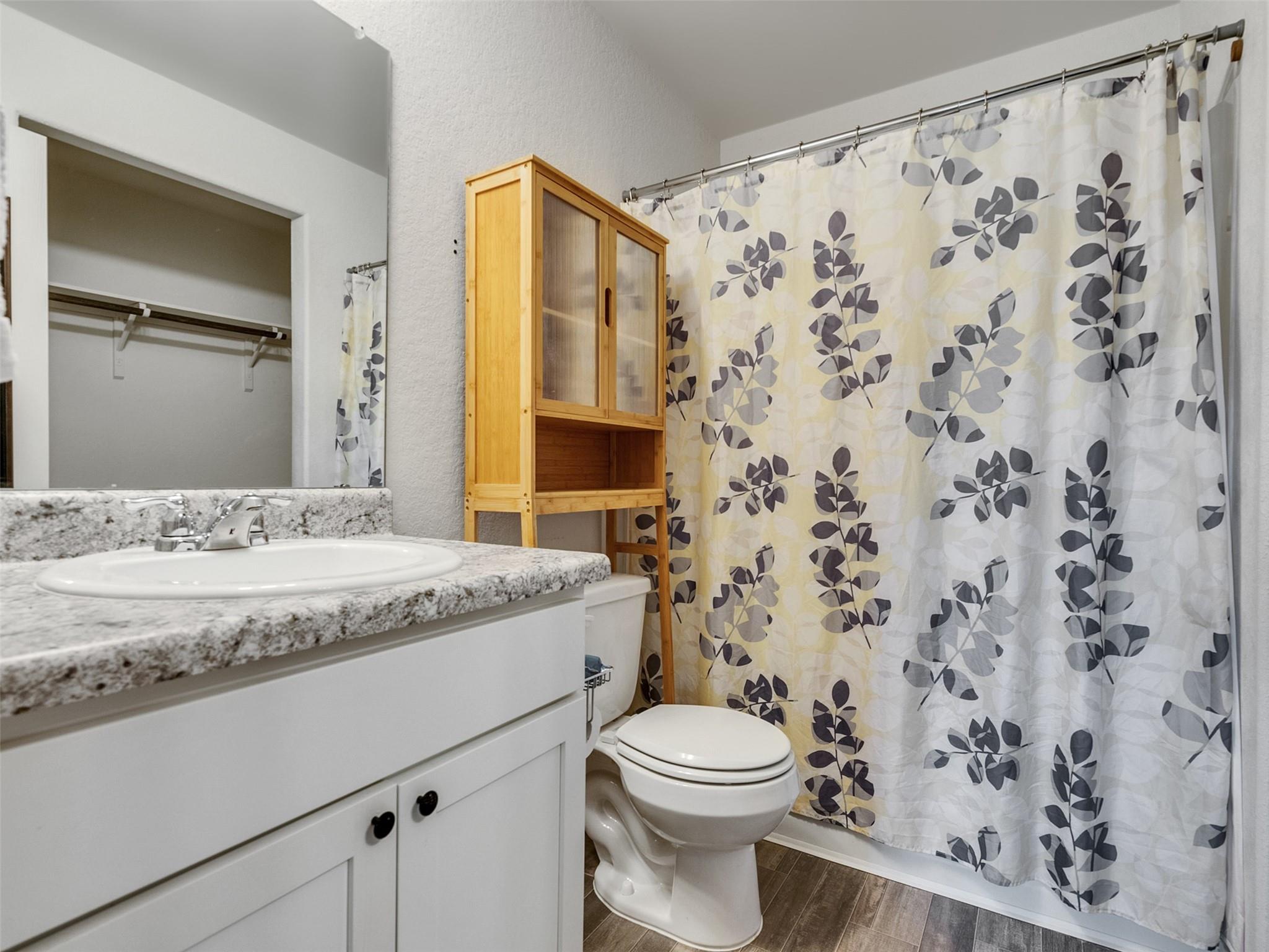 Bathroom with a granite vanity, toilet, and leaf-patterned shower curtain.