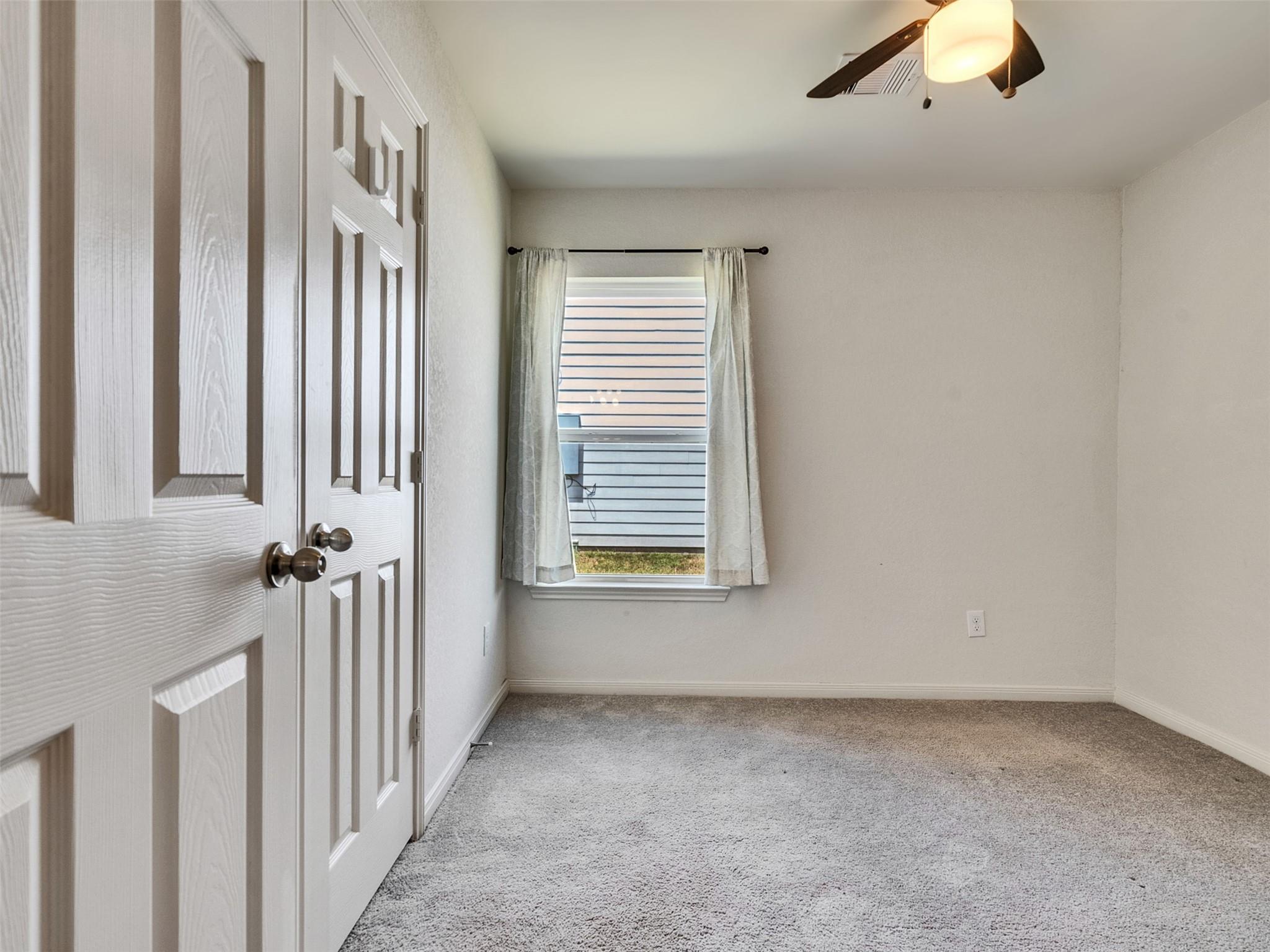 Empty bedroom with gray carpet, white paneled closet doors, and a curtained window.