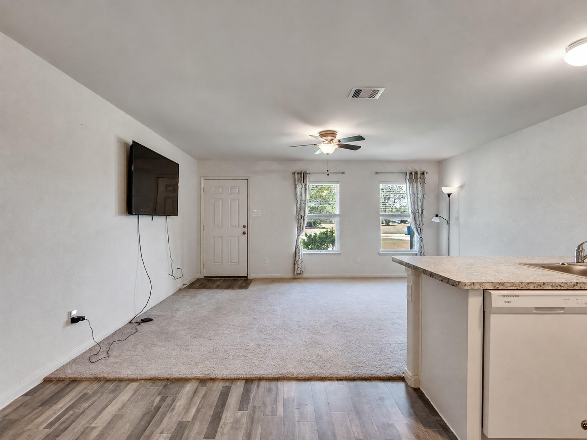 Open-plan living room and kitchen with carpeted seating area, wall-mounted TV, and breakfast bar.