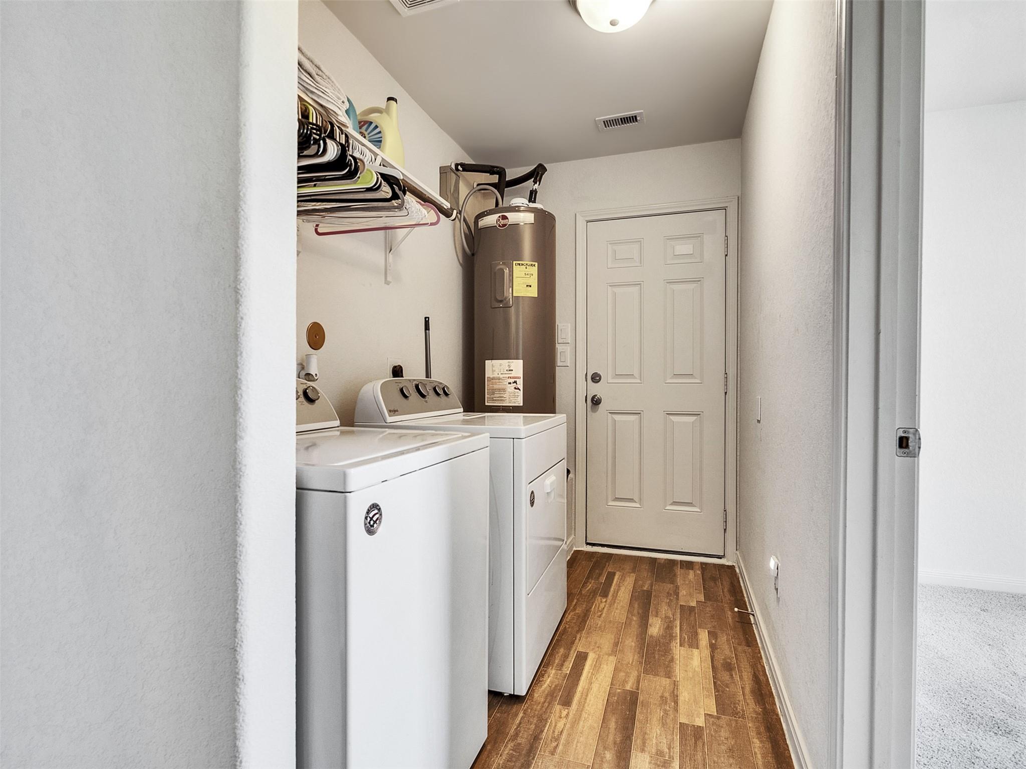 Laundry room with washer, dryer, water heater, and overhead hanging shelves.