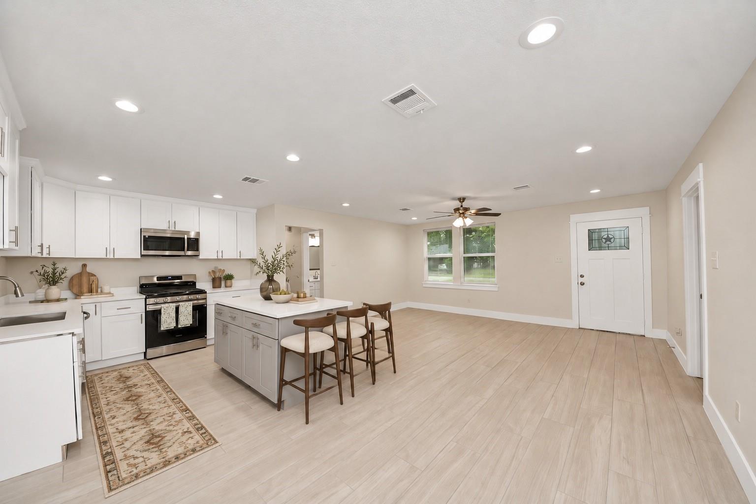 Open kitchen with white cabinets, stainless steel appliances, and an island with bar stools.