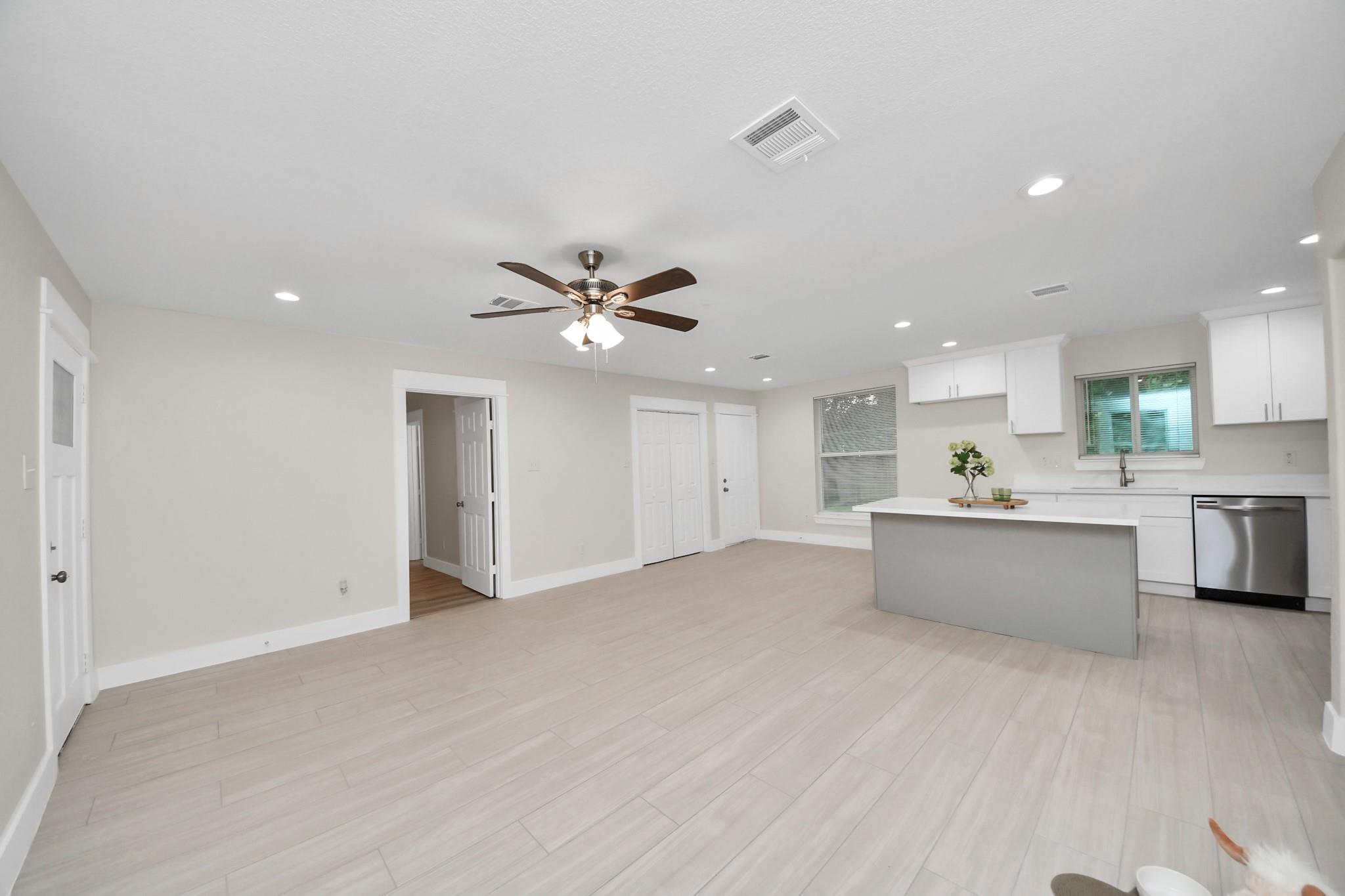 Open kitchen with a gray island, white cabinets, pale tile floors, and a ceiling fan.