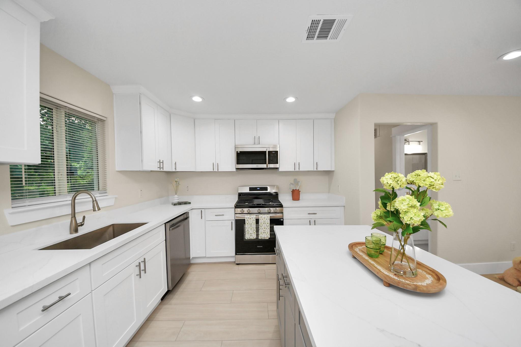 Bright white kitchen with a large island, stainless steel appliances, and flowers on a tray.