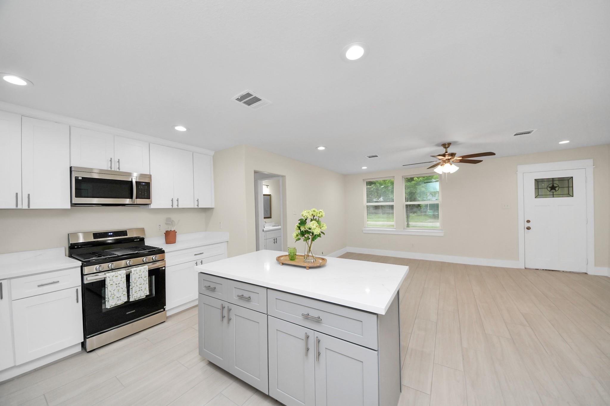 Bright white kitchen with a large island, stainless steel appliances, and light wood-look floors.