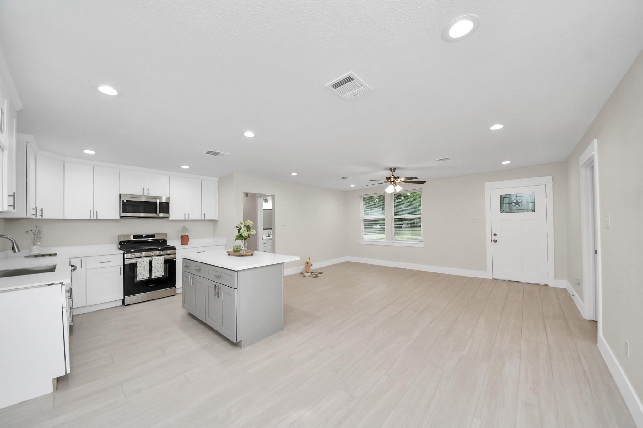 Open-plan kitchen with white cabinetry, stainless steel appliances, and a gray island beside a spacious living area.