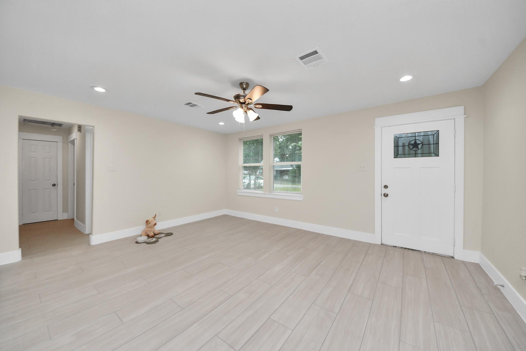 Empty room with pale plank tile, ceiling fan, two windows, and a white door with star-patterned glass.