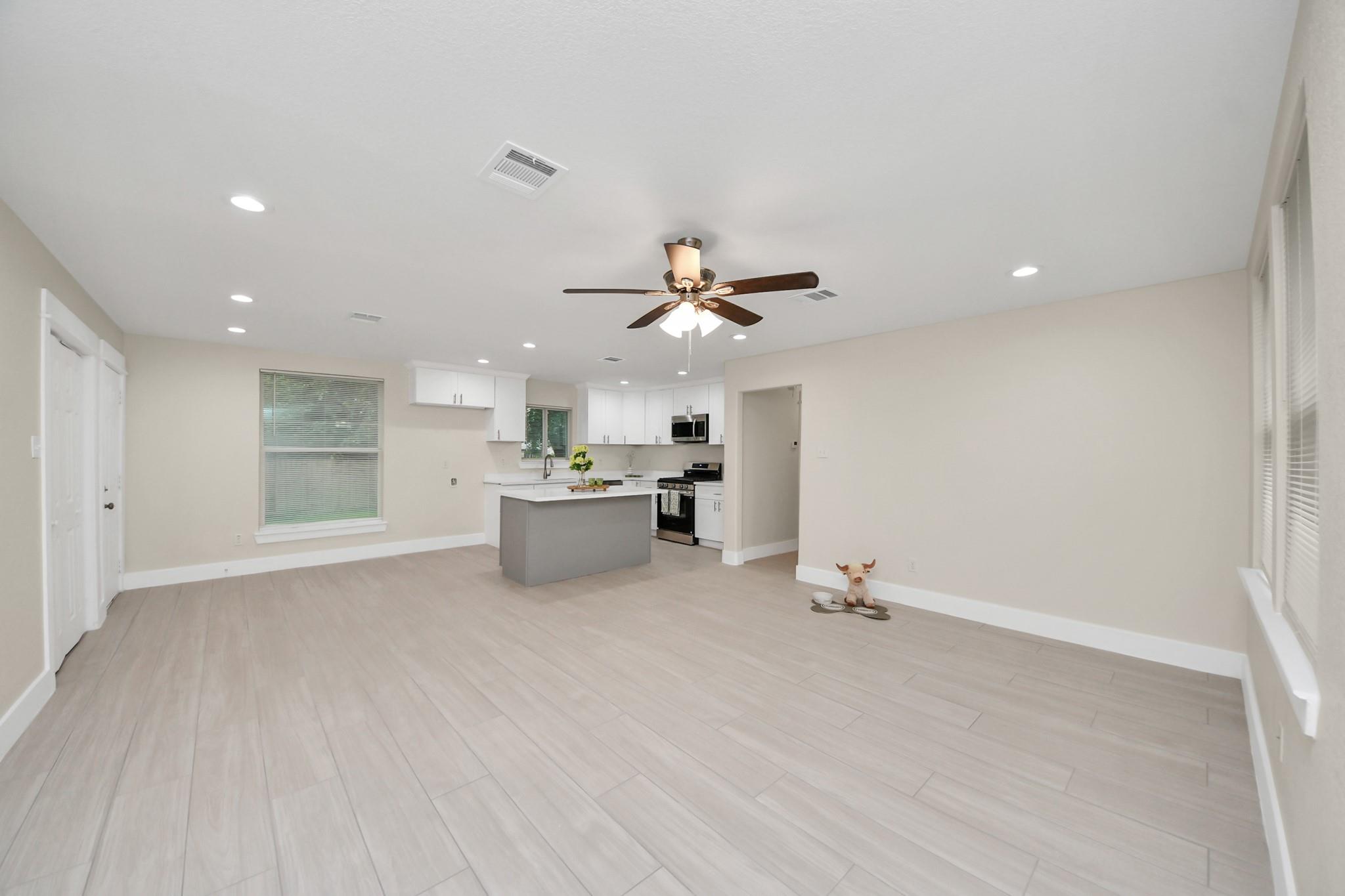Open kitchen and living area with a gray island, white cabinets, and light tile flooring.