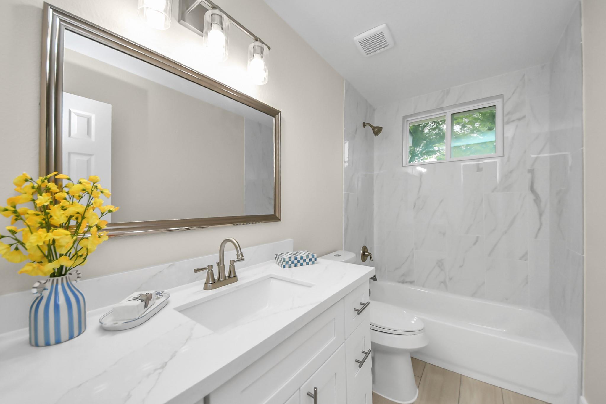 Bathroom with a marble-look vanity and tub-shower surround, plus a window above the tub.