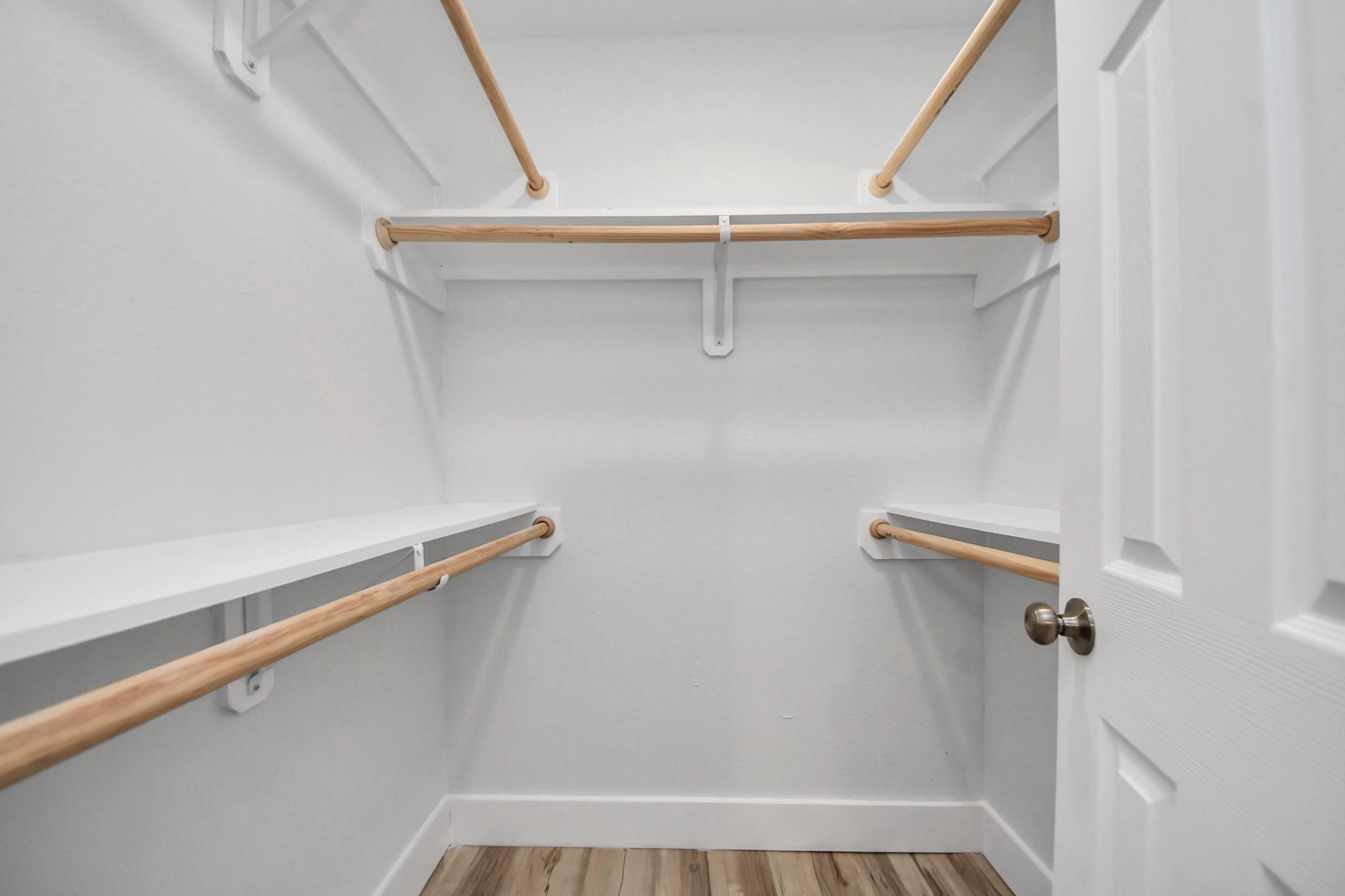 Walk-in closet with white shelving, wooden hanging rods, and wood-look flooring.