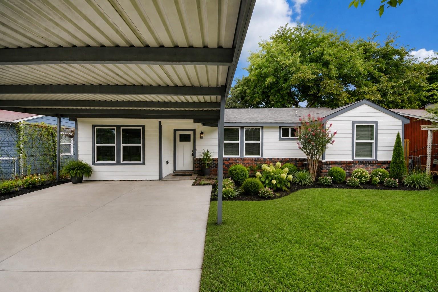 White single-story home with a large covered carport, concrete driveway, and landscaped front yard.