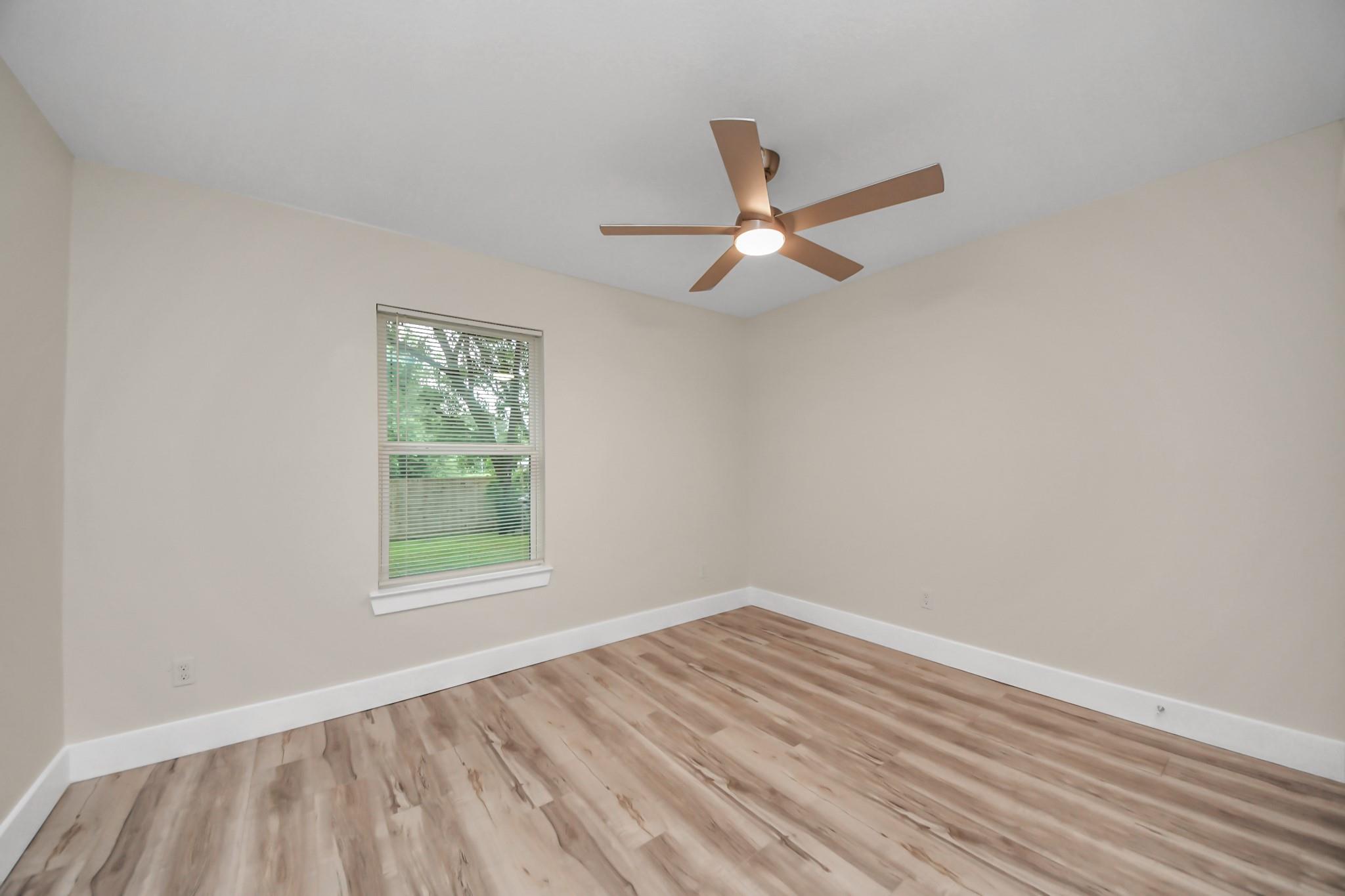 Empty bedroom with wood-look floors, a window with blinds, and a bronze ceiling fan.