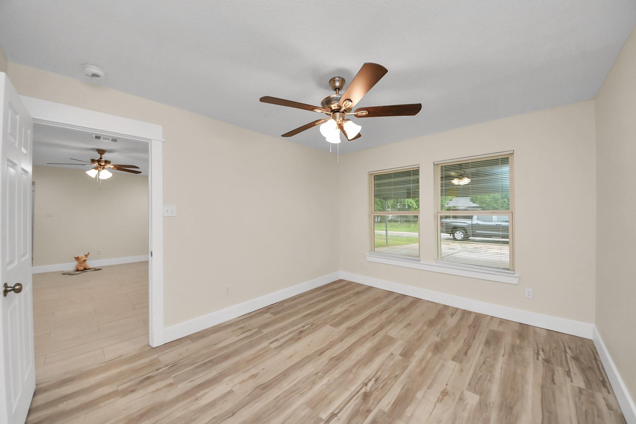 Empty room with wood-look flooring, a ceiling fan, and two windows with blinds.