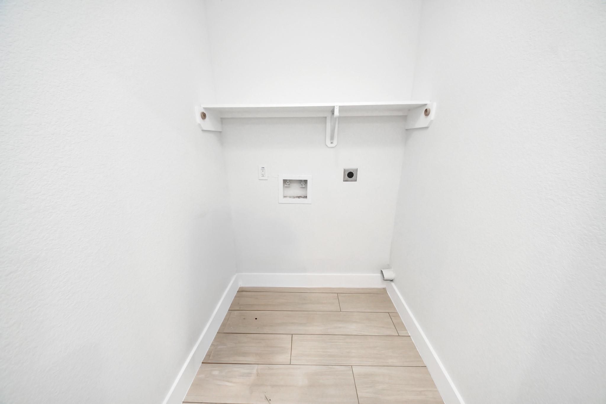 Empty laundry alcove with washer and dryer hookups, a white shelf, and light wood-look tile flooring.