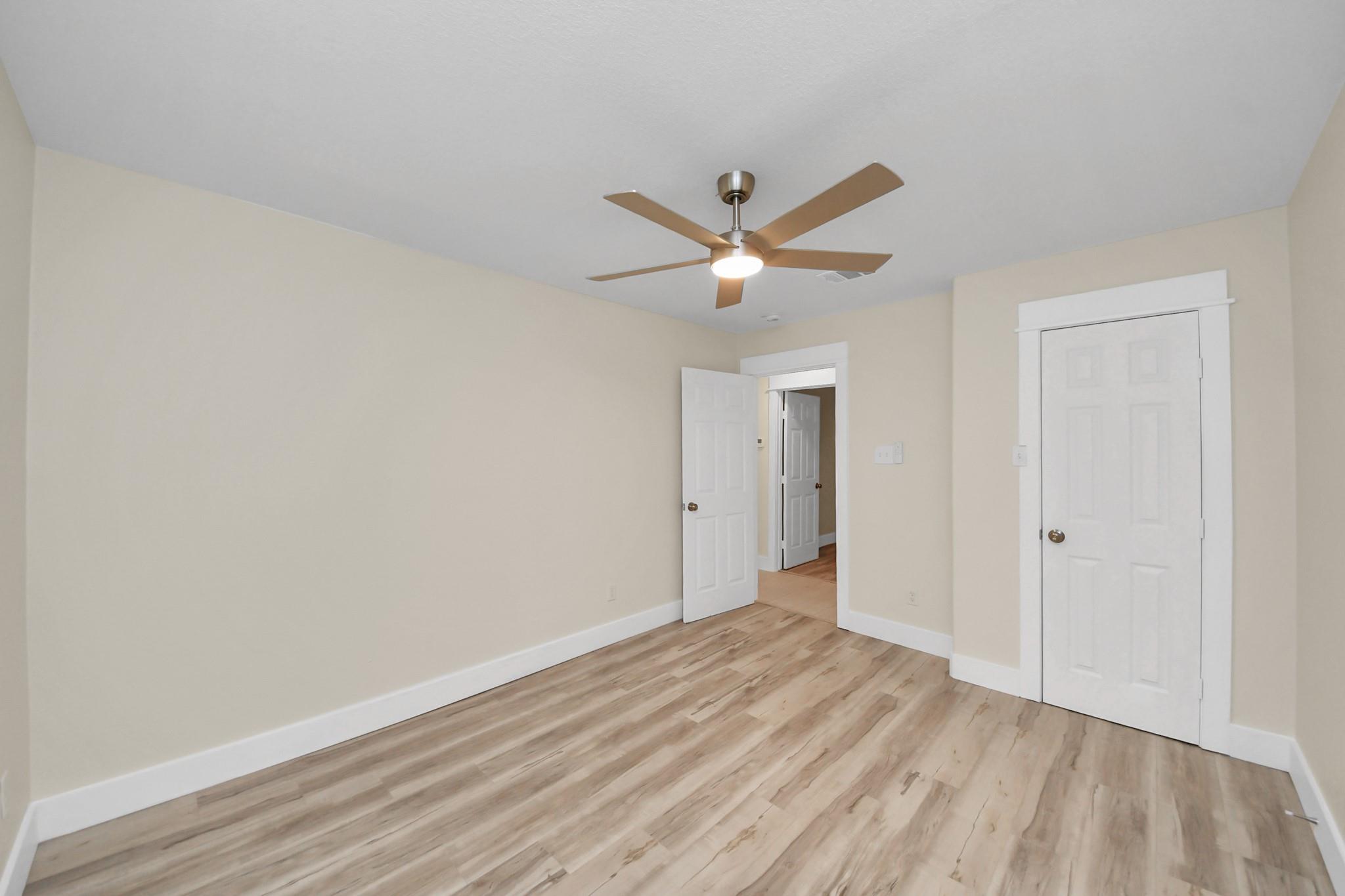 Vacant bedroom with wood-look flooring, a ceiling fan, and white doors.