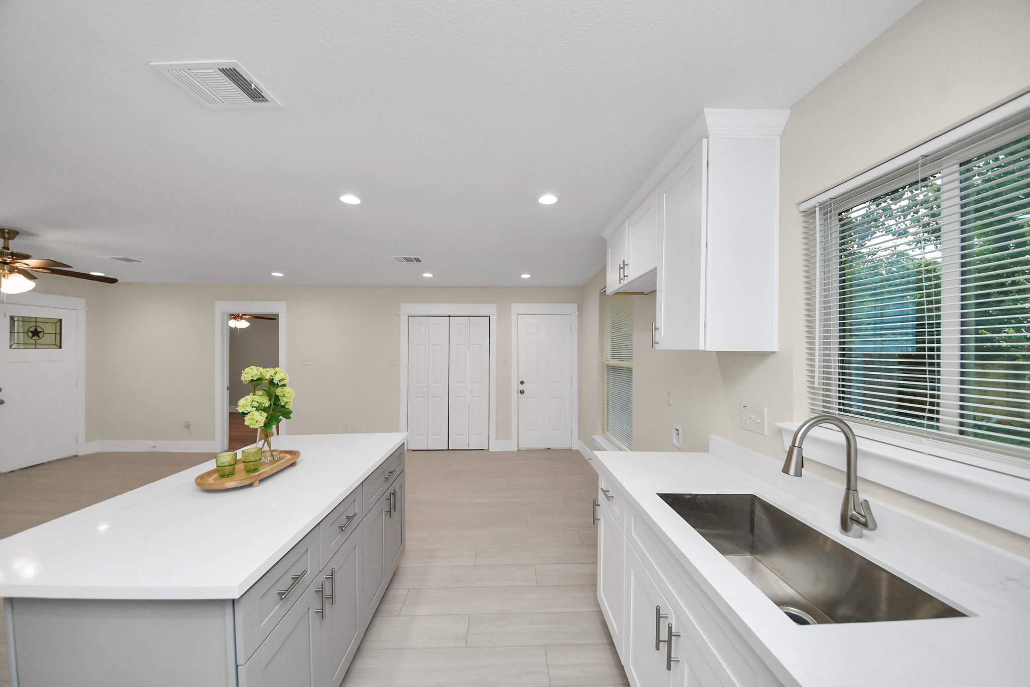 Bright kitchen with a long island, white cabinetry, gray drawers, and a large sink beneath a window.
