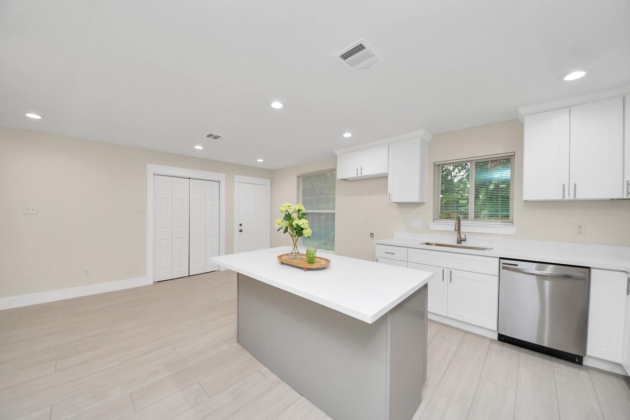 Bright kitchen with white cabinets, a large island, pale tile floors, and a stainless steel dishwasher.