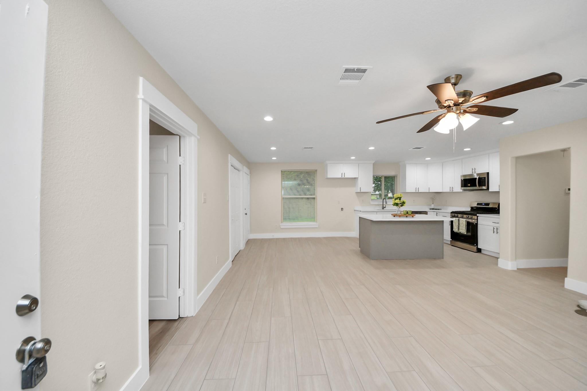 Open-plan kitchen and living area with a gray island, white cabinets, and a dark ceiling fan.