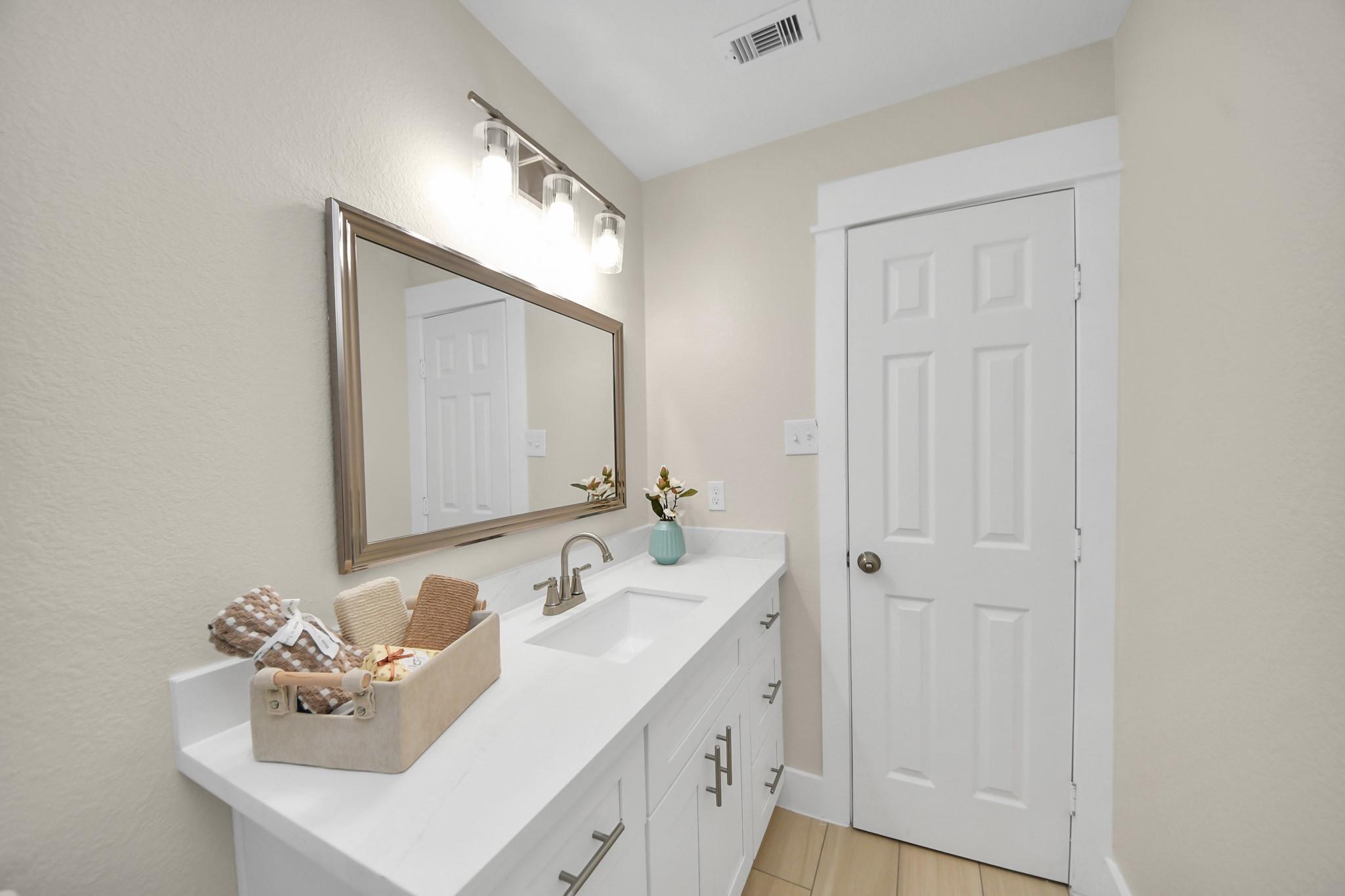 Bathroom vanity with a white sink, large framed mirror, brushed-metal fixtures, and staged towels.