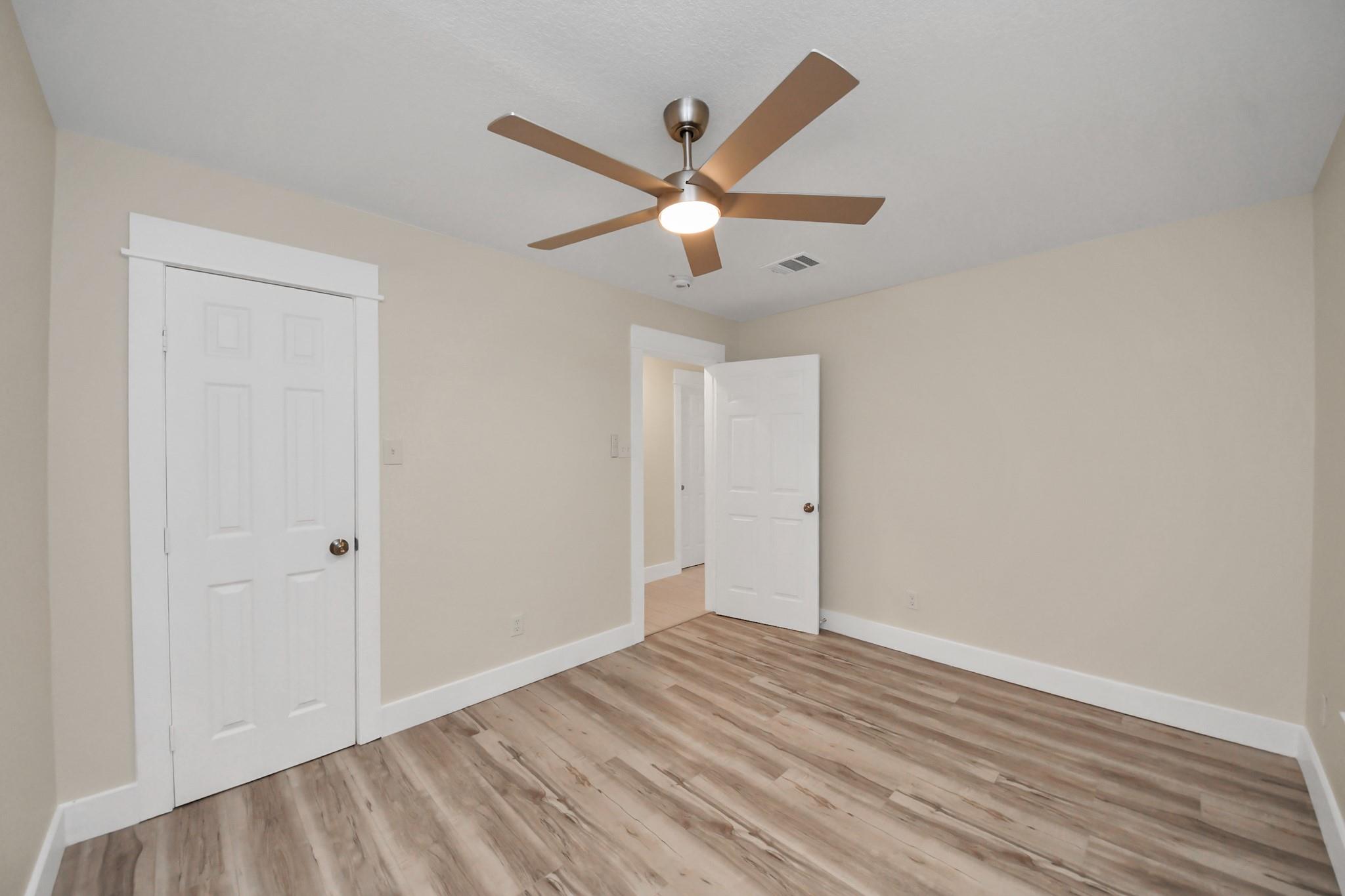 Empty bedroom with wood-look flooring, white closet doors, and a ceiling fan with light.