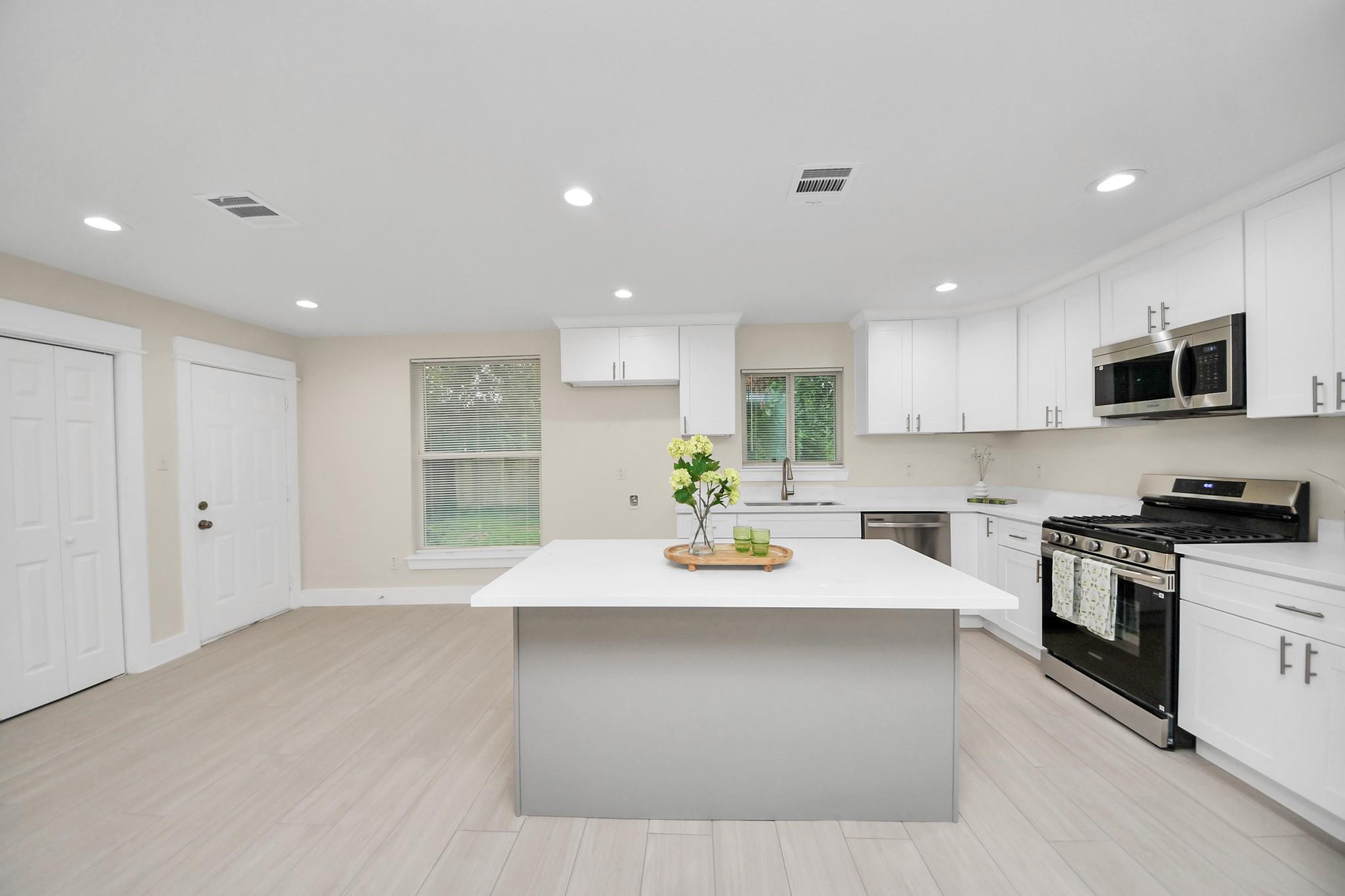 Bright white kitchen with a large island, stainless appliances, and a black gas range.