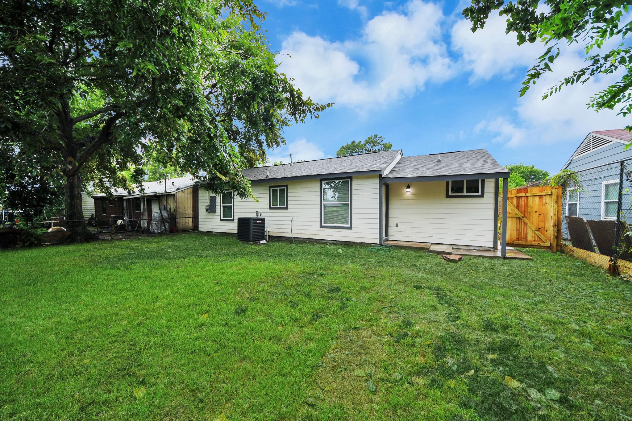 Rear of a single-story house with a covered patio and spacious, tree-shaded backyard.