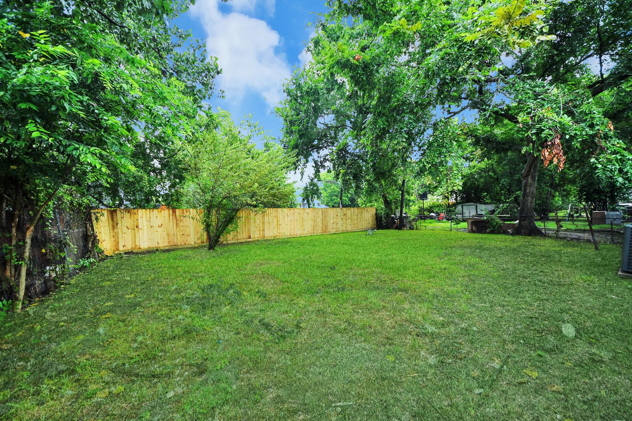 Grassy backyard shaded by mature trees, with wooden privacy fencing and chain-link boundaries.