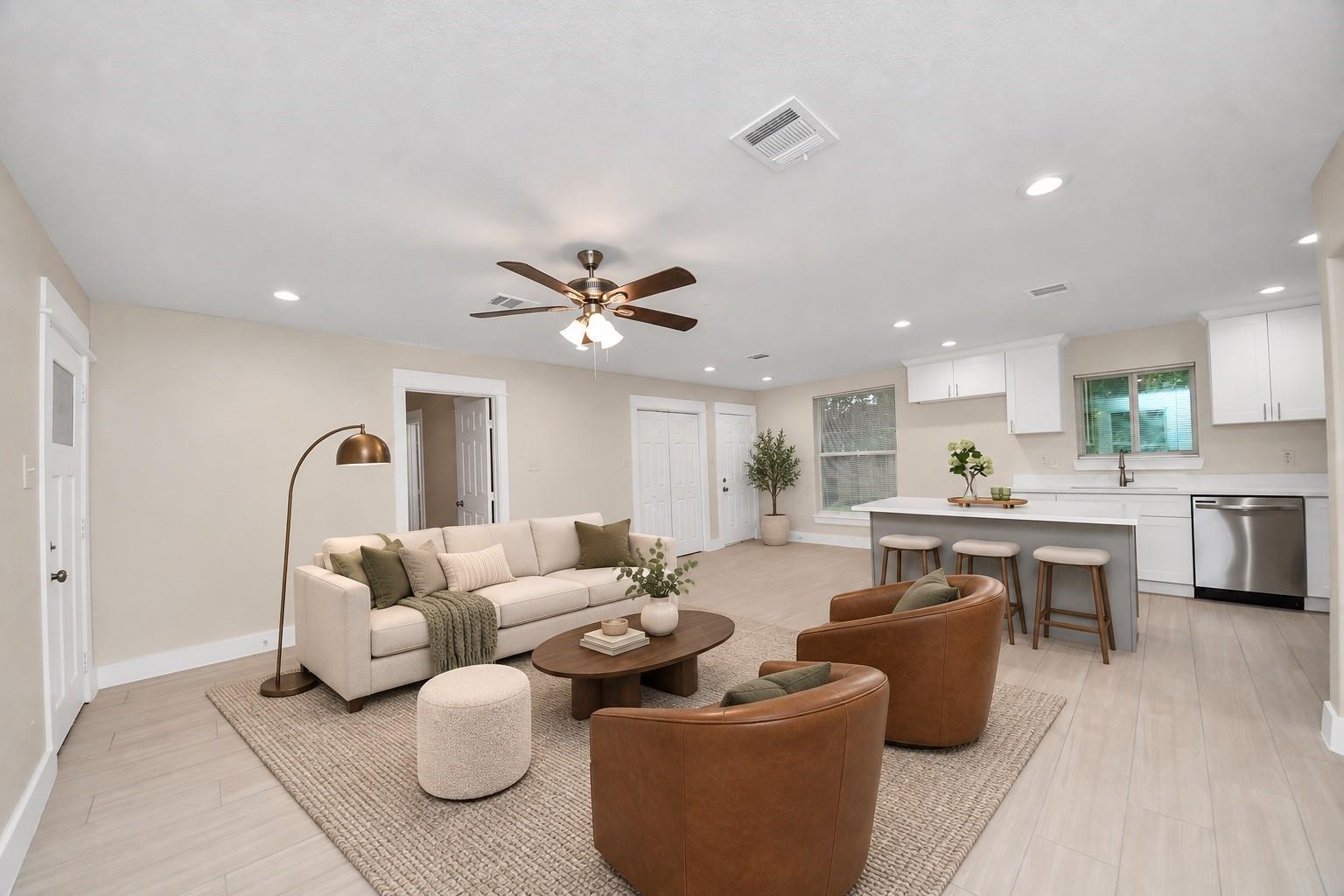 Open-plan living room with cream sofa, leather chairs, and a kitchen island with bar stools.