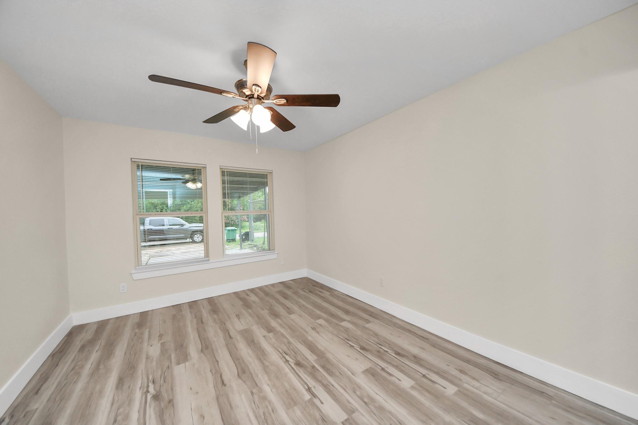 Empty room with wood-look flooring, two windows with blinds, and a ceiling fan with light.