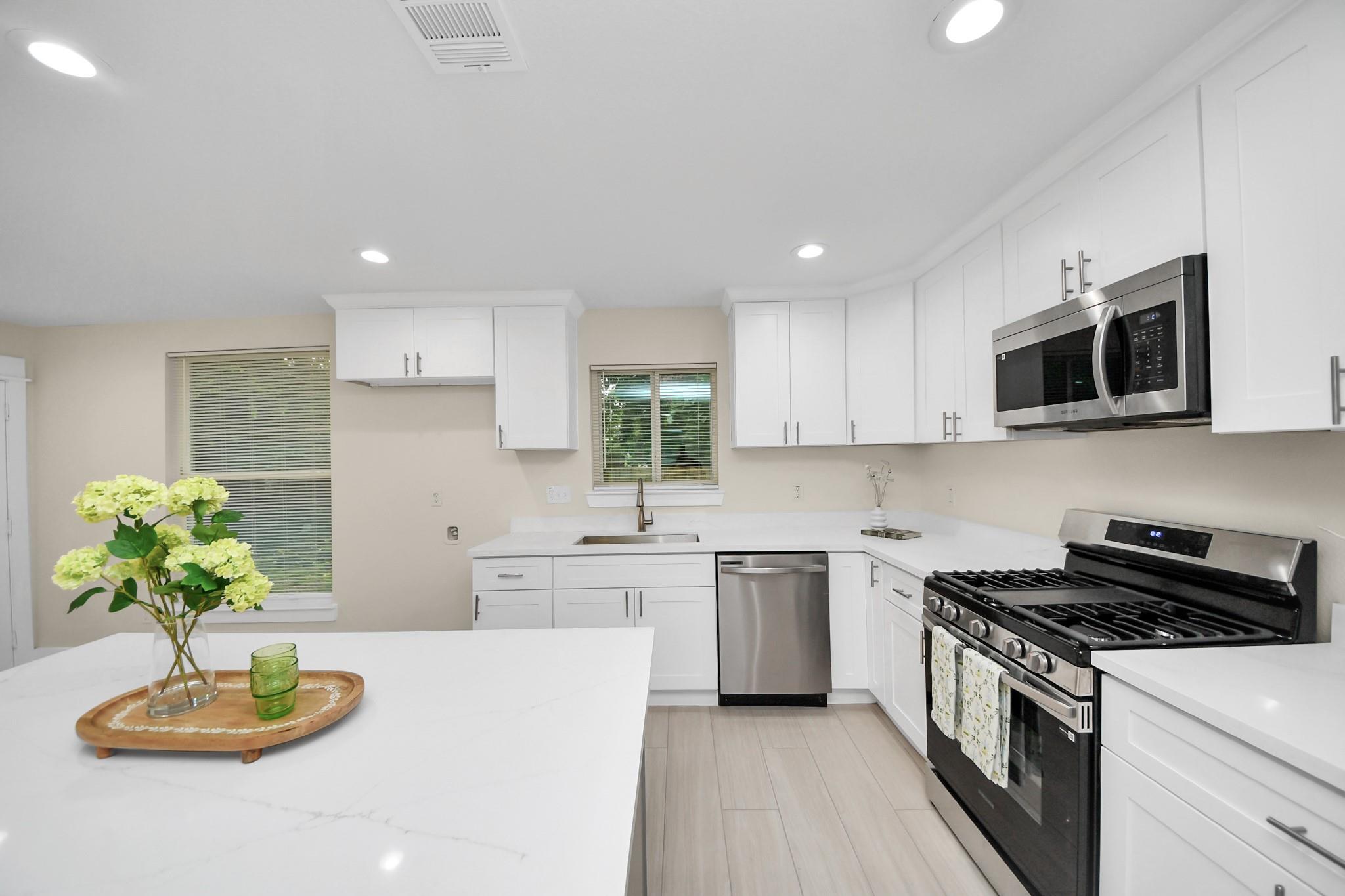 Renovated white kitchen with a large island, stainless steel appliances, and flowers on a tray.