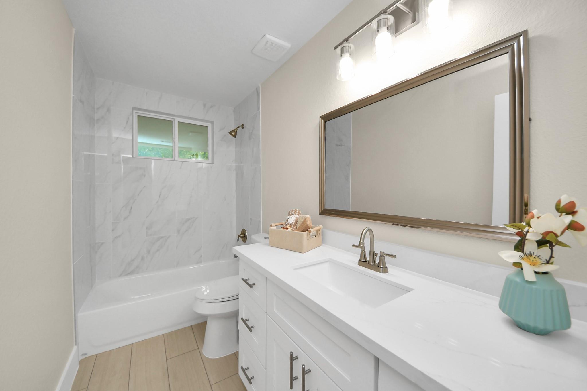 Bathroom with a white vanity and large mirror beside a marble-look tiled bathtub.